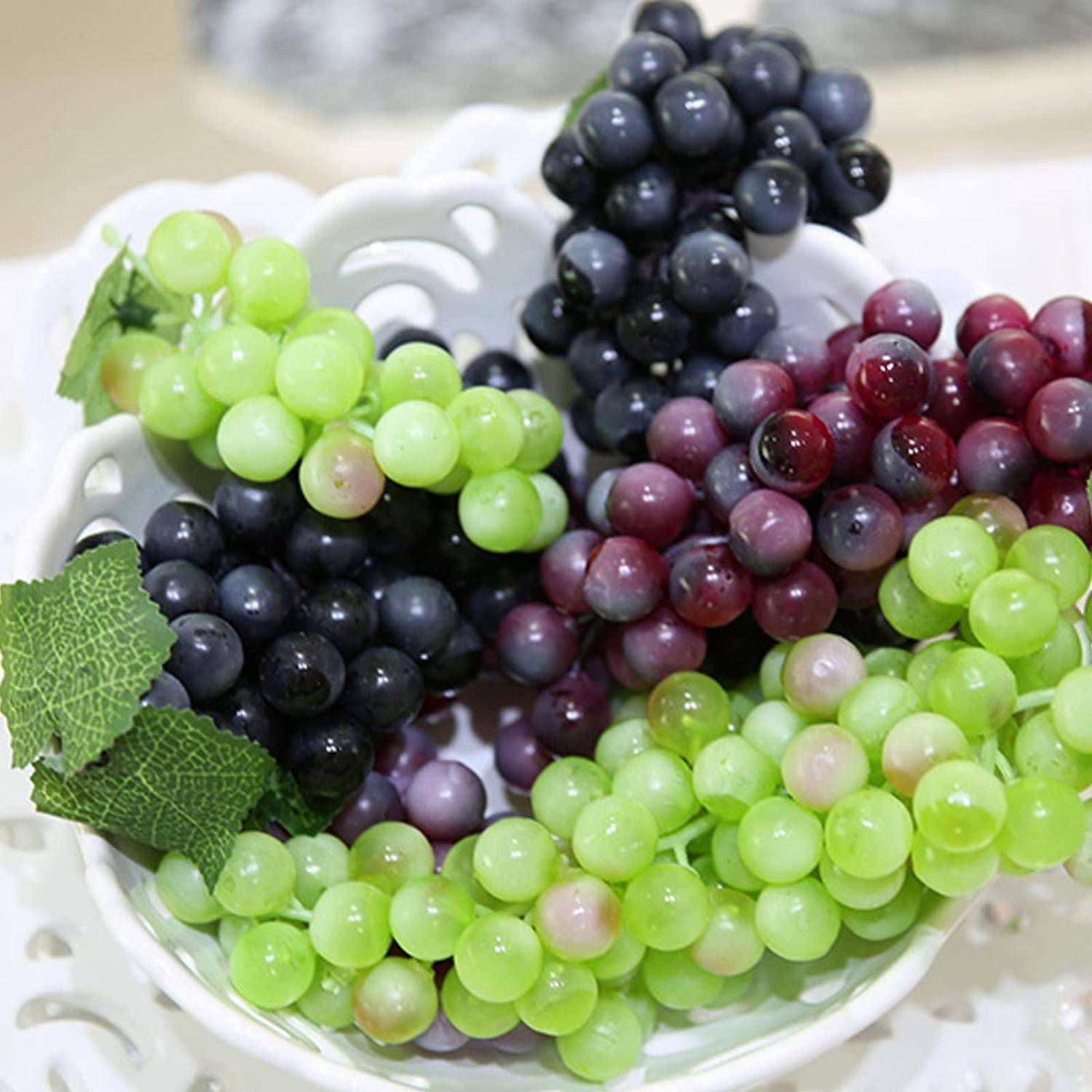 Weiße Schale gefüllt mit Traubentrauben in Grün, Lila und Schwarz, mit ein paar Blättern auf der Seite.