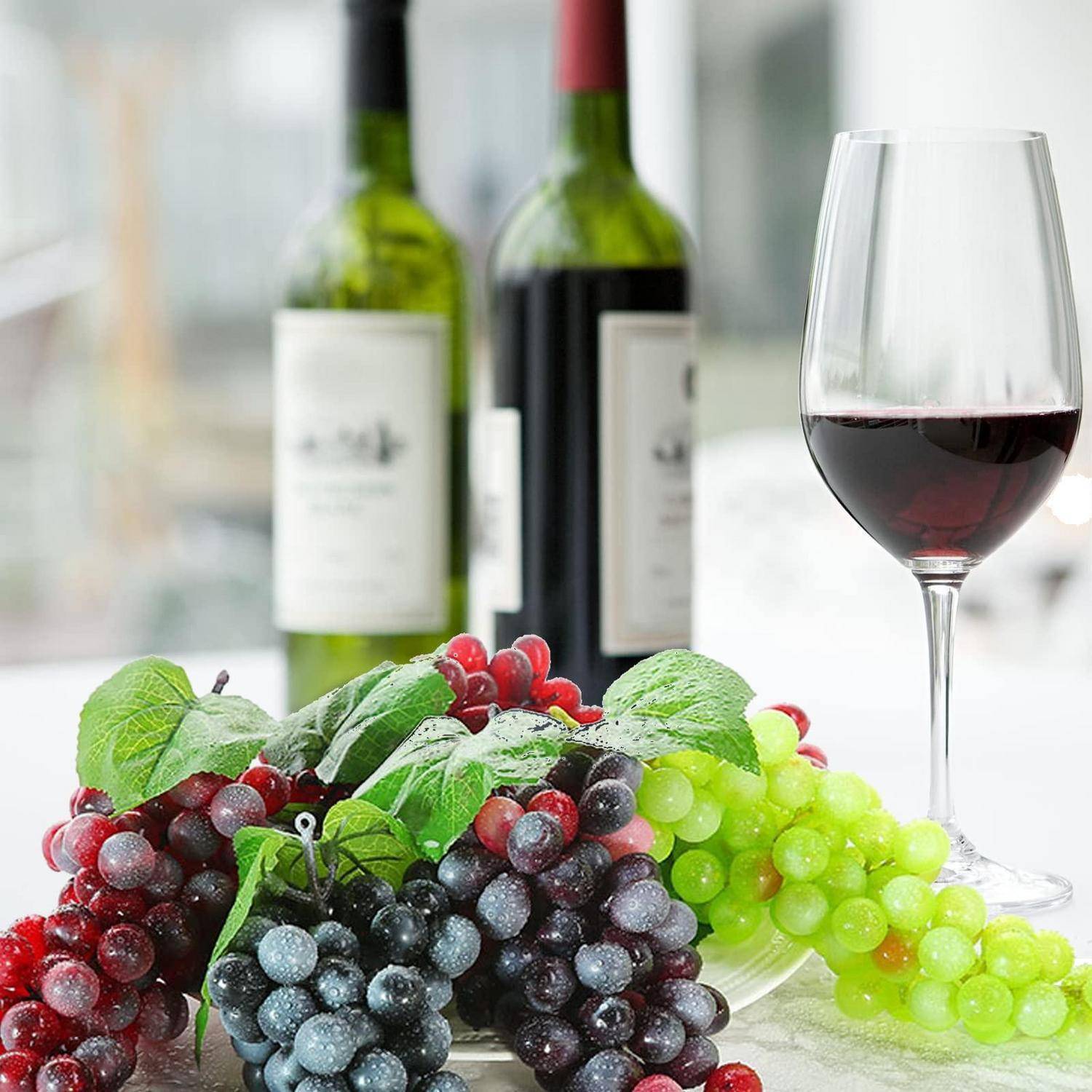 Weinglas mit Rotwein neben Weinflaschen und gemischten Trauben, was auf eine Weinverkostung oder Weinkombination hindeutet.