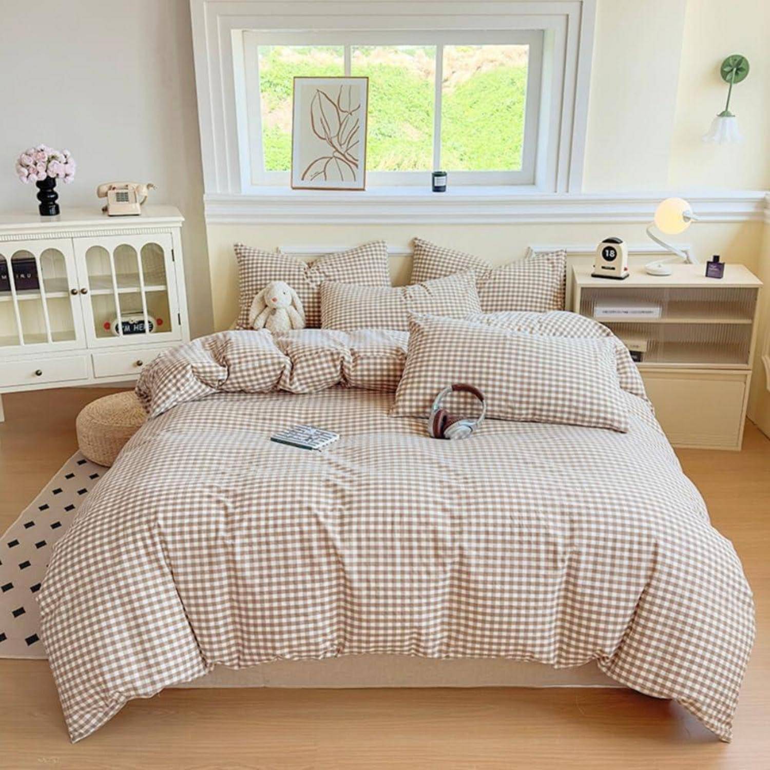 Gemütliches Schlafzimmer mit einem Bett, das mit beige karierter Bettwäsche bezogen ist, Kissen, einem Teddybär, einem Nachttisch, einem Schrank und einem Fenster über dem Kopfteil.