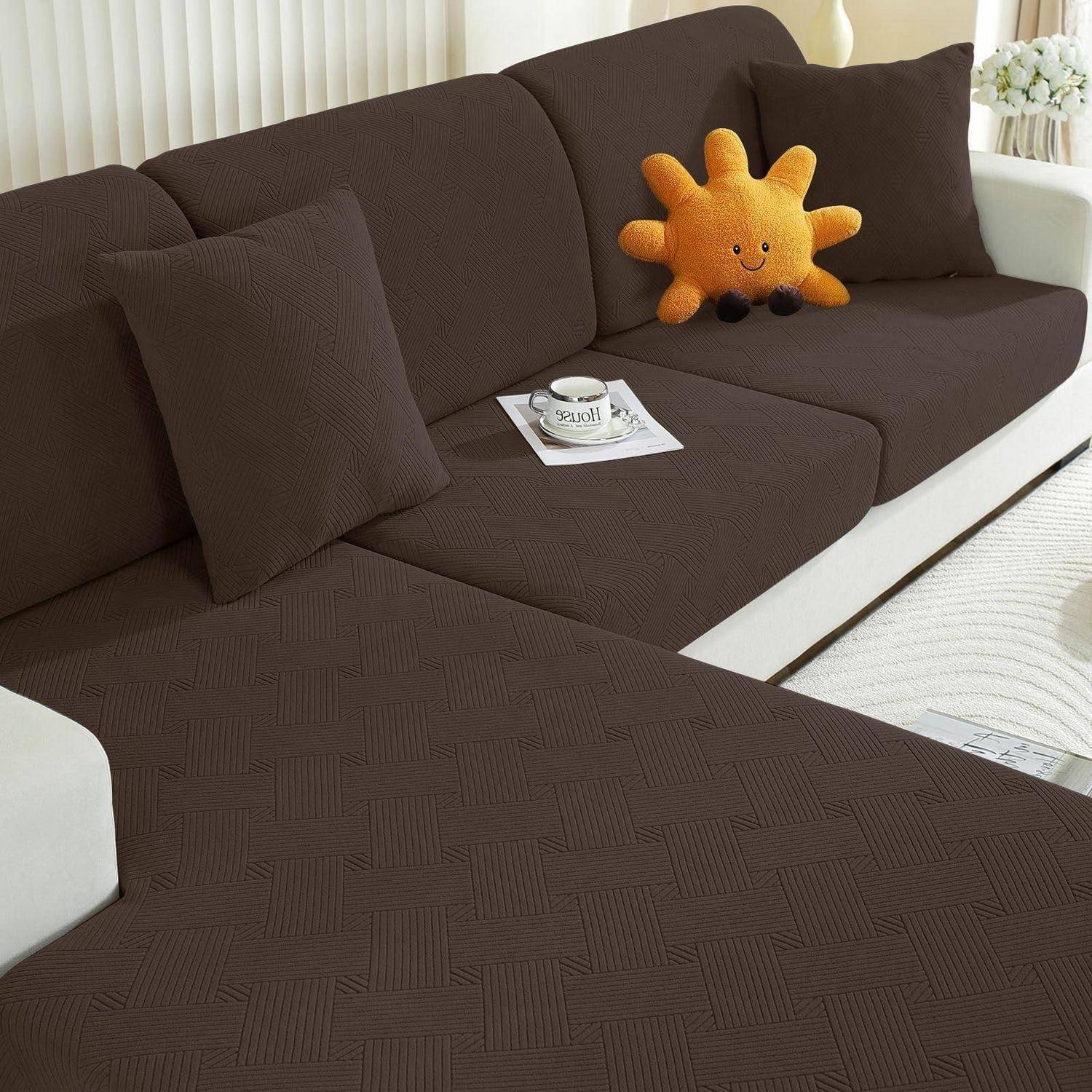 Braunes Ecksofa mit passenden Kissen, orangefarbenes sonnenförmiges Plüschtier und ein kleines Tablett mit einer Tasse auf dem Sitz in einem hellen Wohnzimmer.