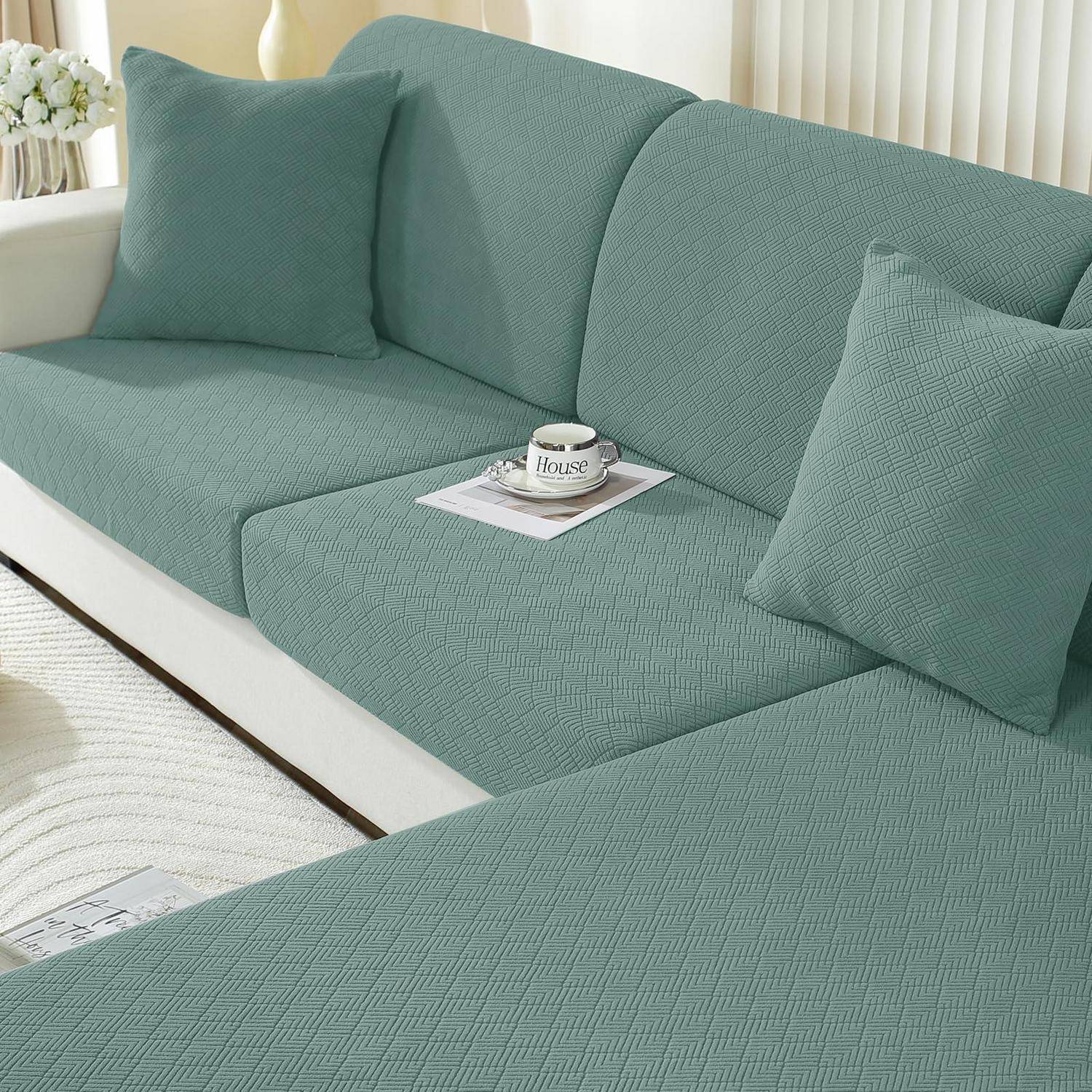 Teal-gepolstertes Sofa mit passenden Kissen in einem hellen Raum; eine Tasse und ein Magazin liegen auf dem Sitz.