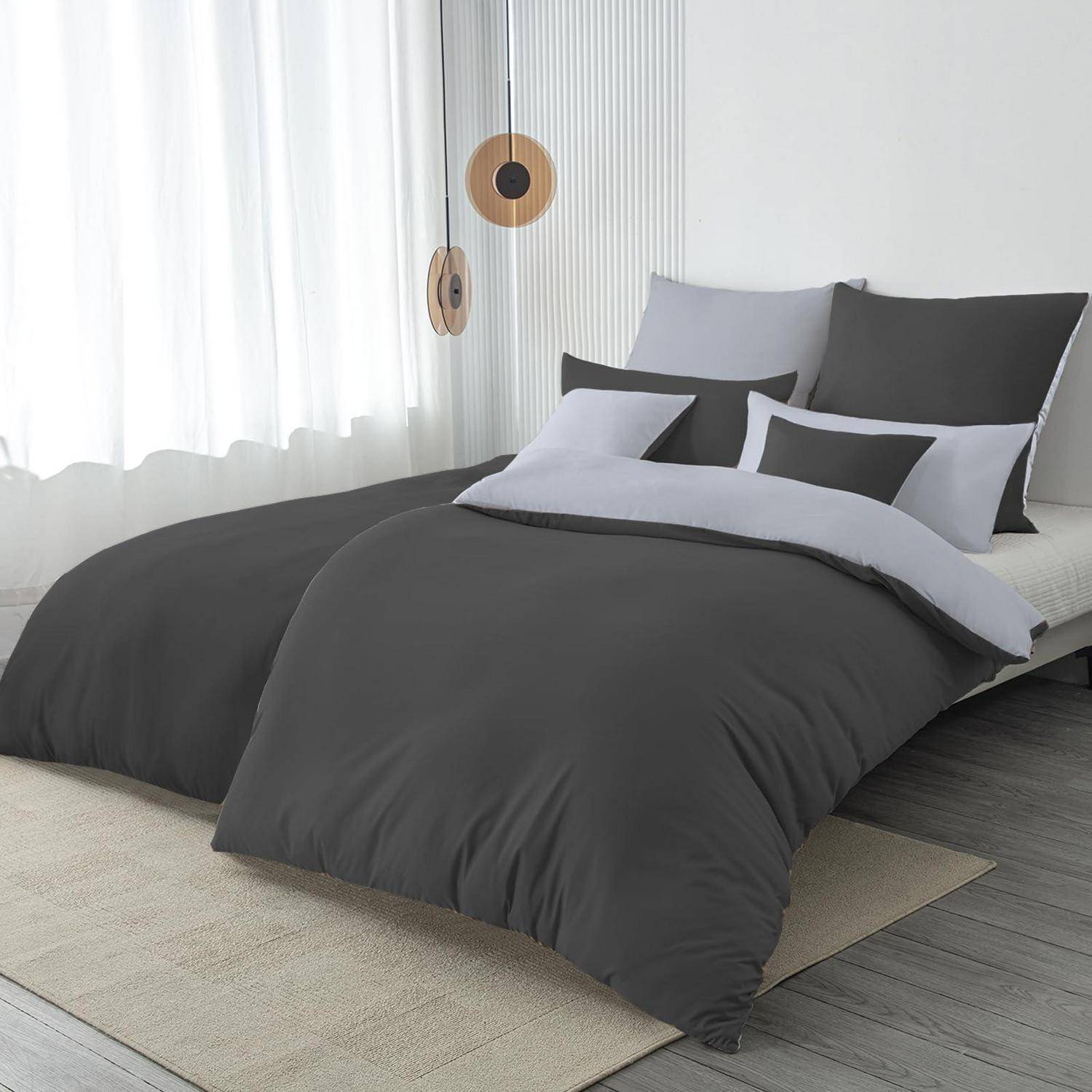 Modernes Bett mit dunkelgrauer Bettwäsche, hellgrauen und schwarzen Kissen in einem hellen, minimalistischen Schlafzimmer.