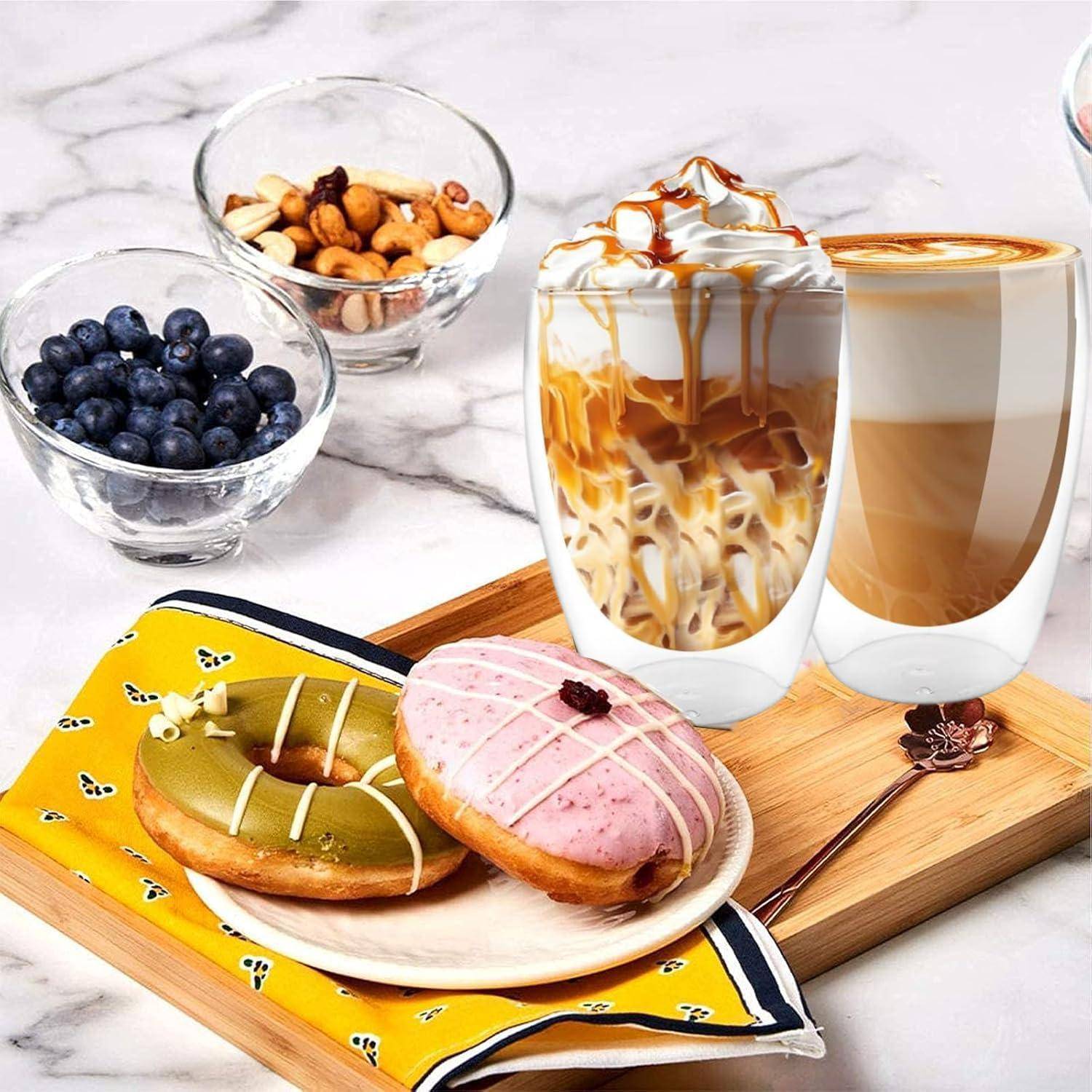 Zwei Eiskaffees mit Karamelldrizzle und zwei glasierte Donuts auf einem Teller, mit Schüsseln voller Blaubeeren und Nüssen auf einer Marmortheke.