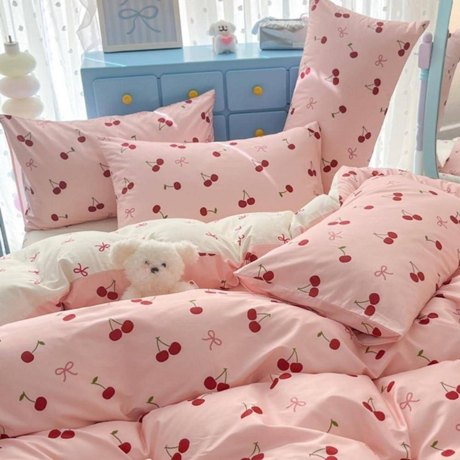 Ein Bett mit rosa Kirschmuster-Bettwäsche und Kissen, mit einem kleinen weißen Plüschhund, der in der Mitte hervorlugt.