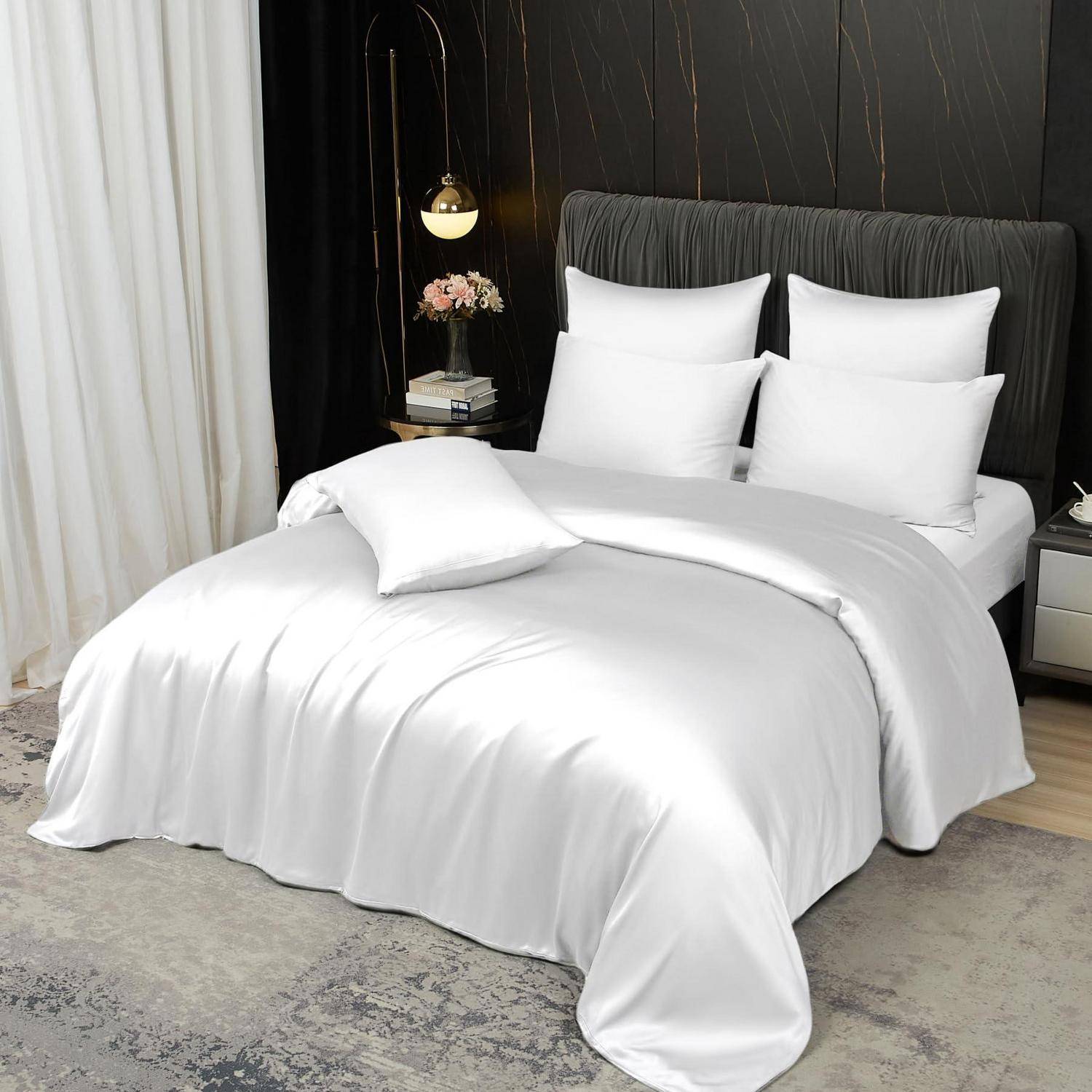 Weißes Bettwäsche-Set auf einem ordentlich gemachten Bett in einem modernen dunklen Schlafzimmer, mit Kissen, Steppdecke, Nachttischlampe und Nachttischen.