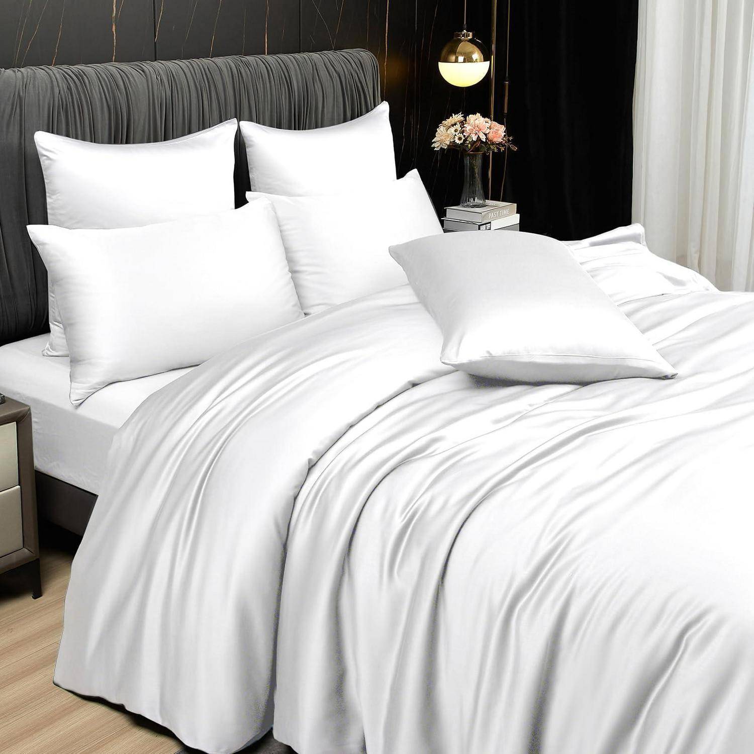 Ordentlich gemachtes Bett mit weißer Bettwäsche und Kissen in einem modernen Schlafzimmer, mit grauem gepolstertem Kopfteil und Nachttischlampe.