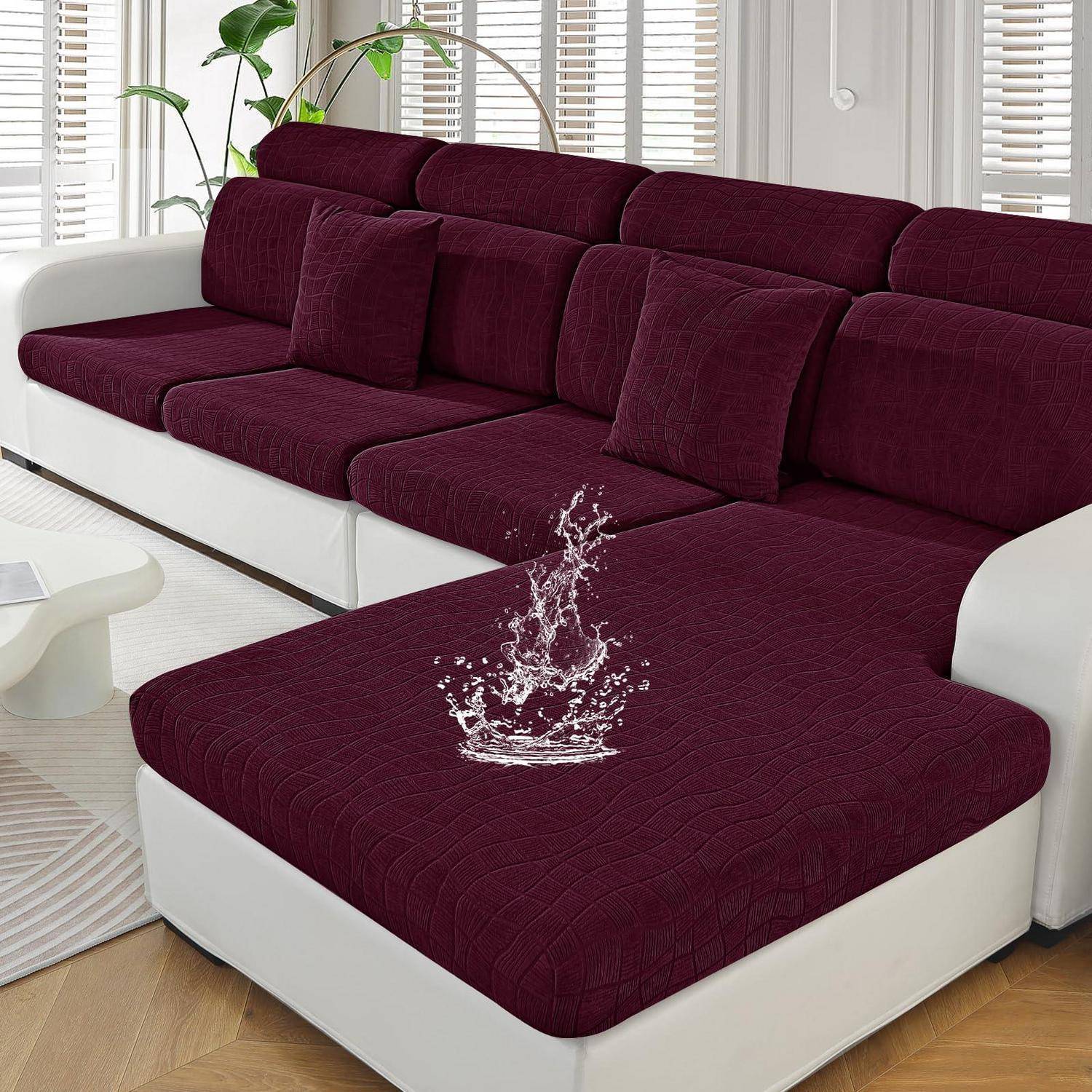 Modernes Ecksofa mit bordeauxroten Kissen und weißem Untergestell; der mittlere Sitzplatz zeigt Wasser, das auf den Stoff spritzt, was auf eine wasserabweisende Oberfläche hindeutet.