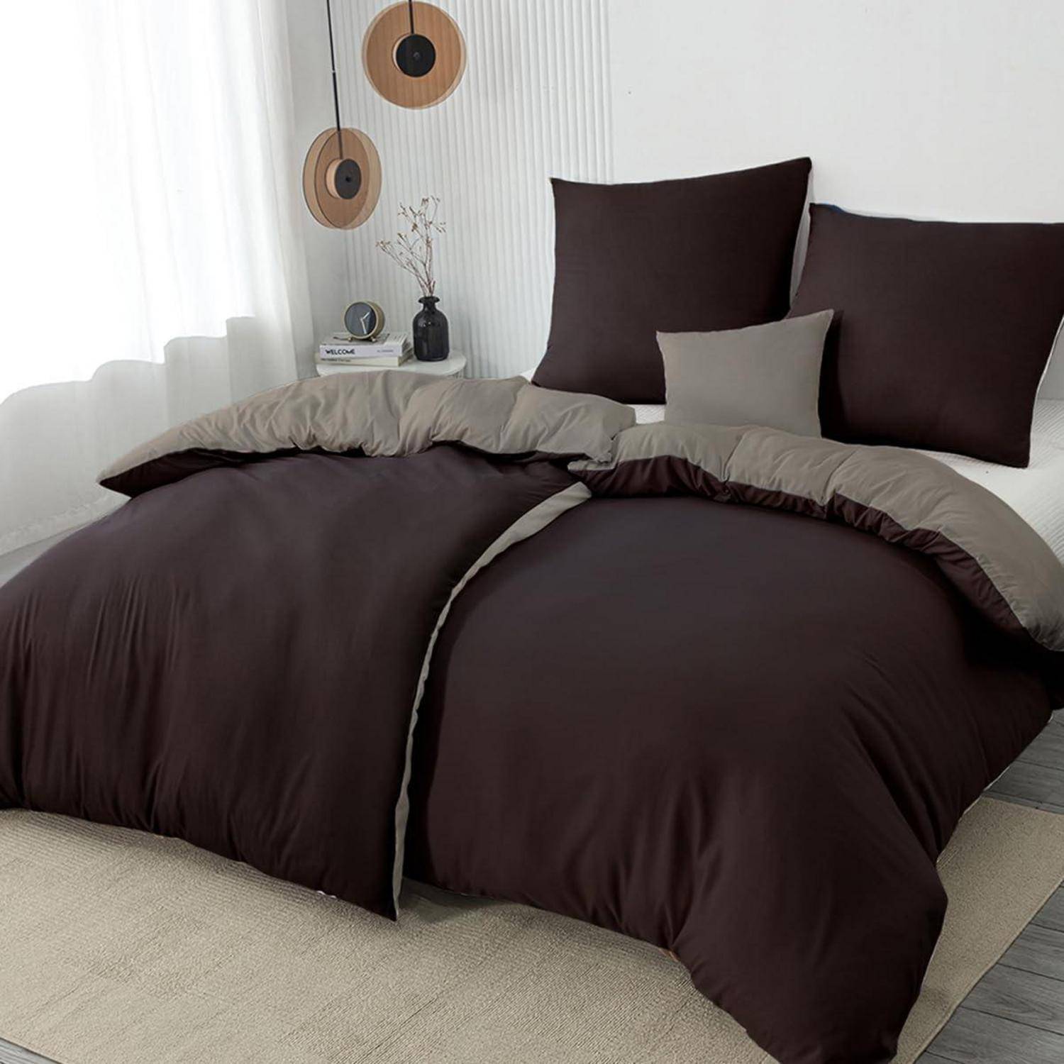 Ein sauber gemachtes Bett mit dunkelbrauner und taupefarben Bettwäsche, zwei großen Kissen und kleiner Wanddekoration in einem hellen, minimalistischen Schlafzimmer.
