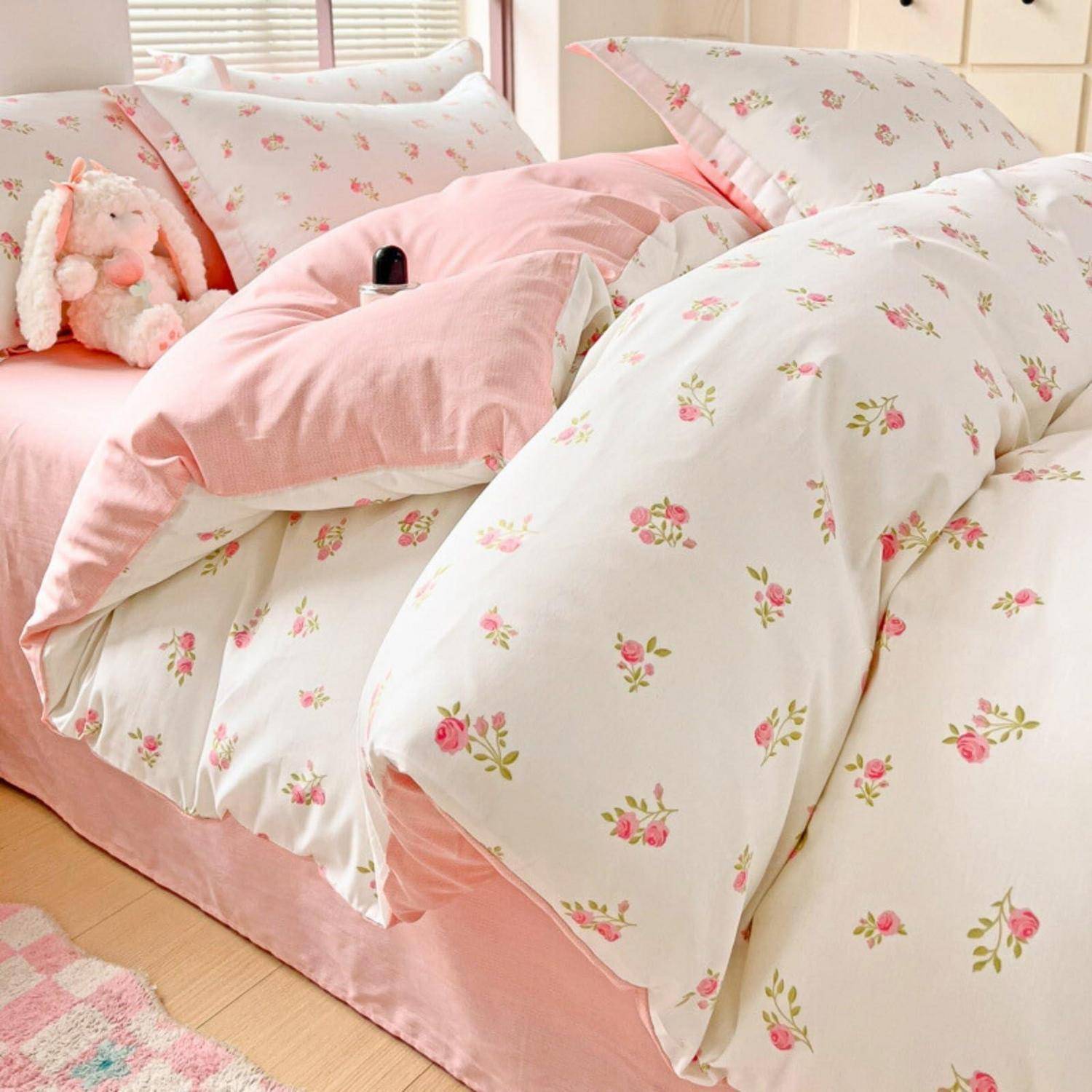 Rosa Blumenbettwäsche mit Kissen und einem kuscheligen Kaninchen auf einem ordentlich gemachten Bett in einem hellen Schlafzimmer.