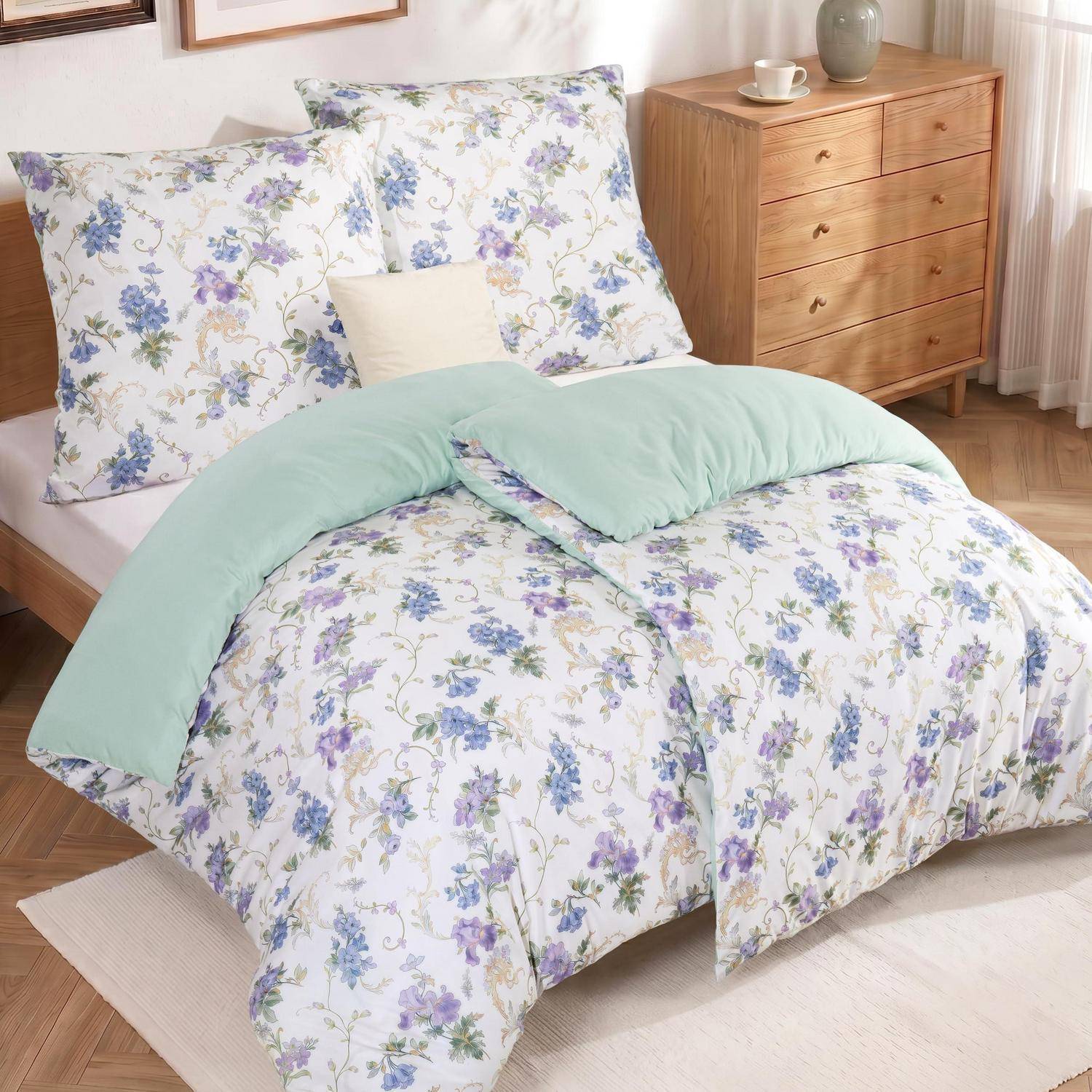 Bett mit weißer Blumenbettwäsche, mintgrüner Decke und passenden Kissen in einem ordentlichen Schlafzimmer mit einer Holzkommode.