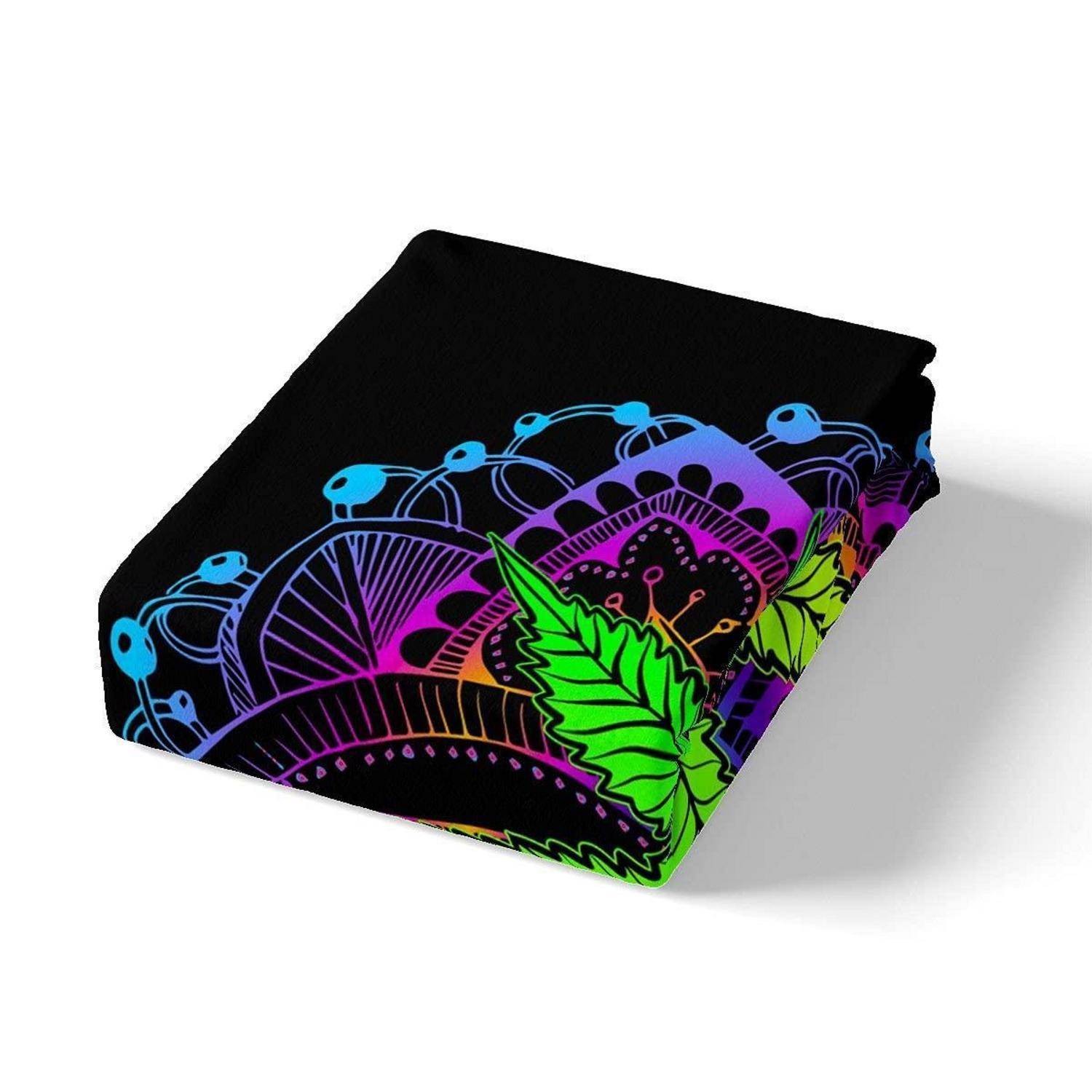 Gefaltete schwarze Decke mit leuchtendem Neon-Mandala- und Blattmuster auf weißem Hintergrund.