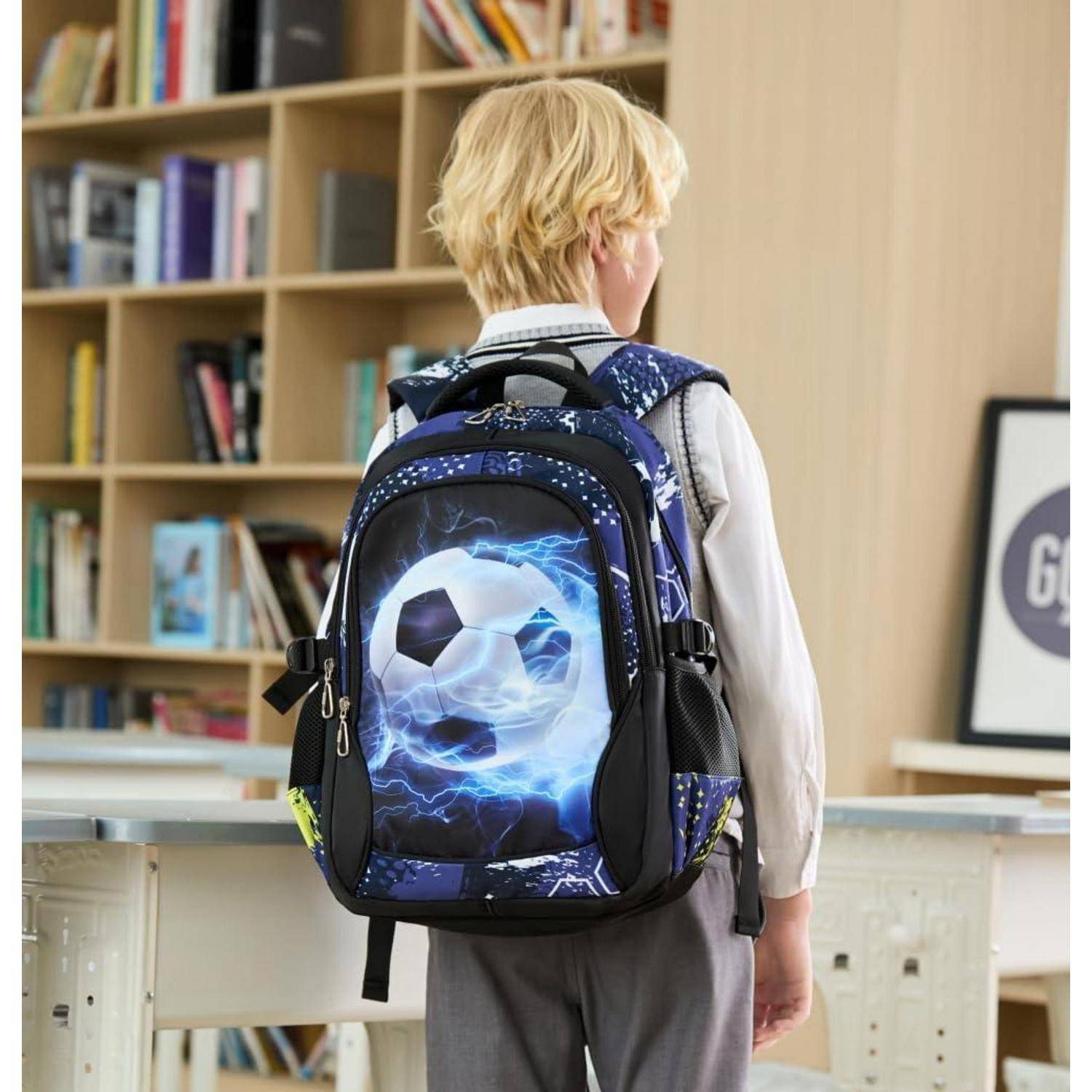 Junger Junge von hinten gesehen, der einen großen Rucksack mit einem leuchtenden Fußballdesign trägt und in einer Bibliothek oder einem Klassenzimmer steht.
