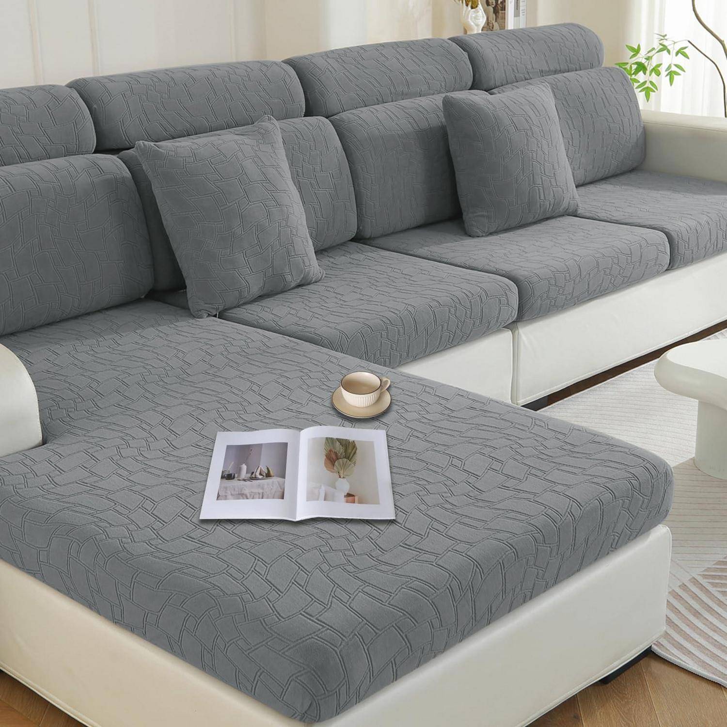 Graues Ecksofa mit passenden Kissen und aufgeschlagenem Buch auf der Chaiselongue, dargestellt in einem hellen Wohnzimmer.
