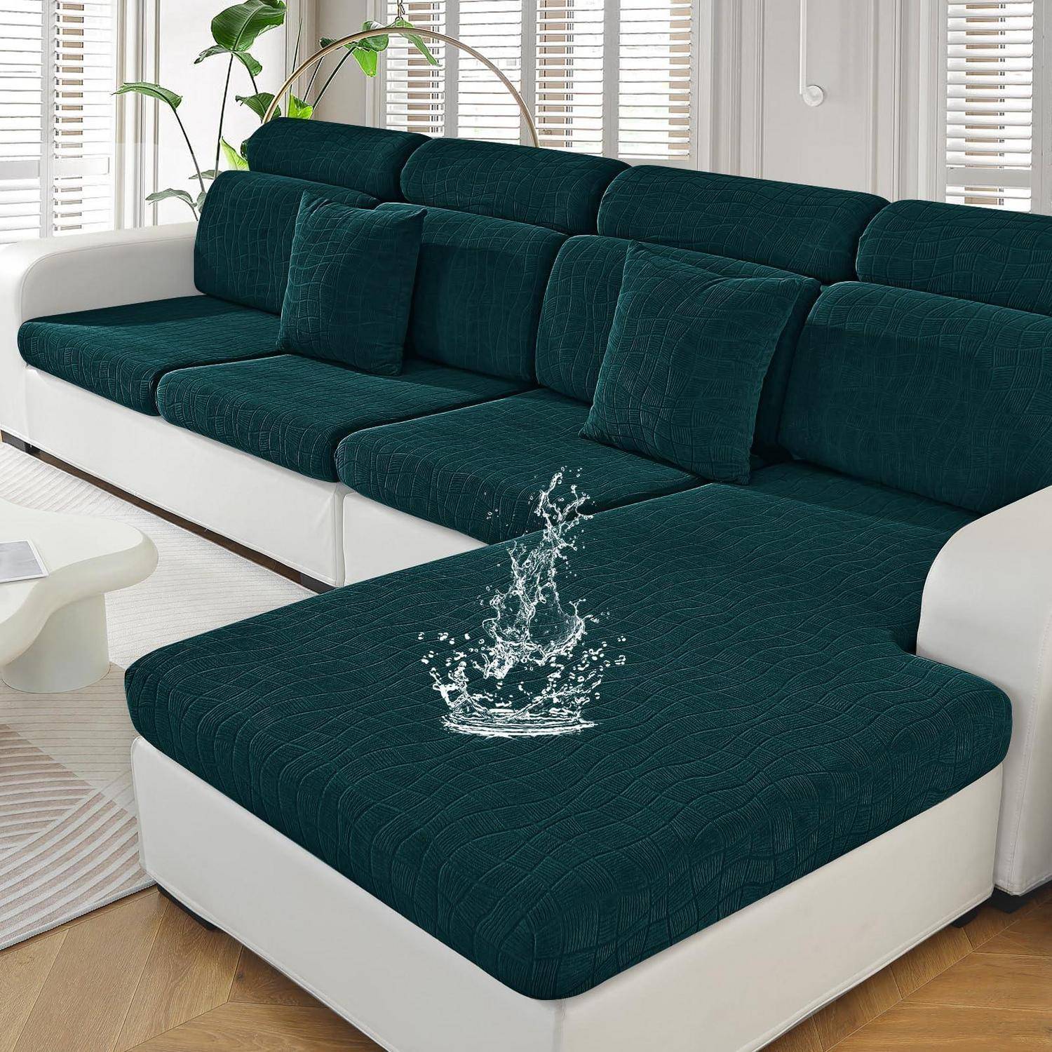Dunkelgrünes Ecksofa mit weißer Basis und passendem Hocker in einem hellen Wohnzimmer; Wasserspritzer auf dem Hocker unterstreichen die wasserabweisende Stoffbeschaffenheit.