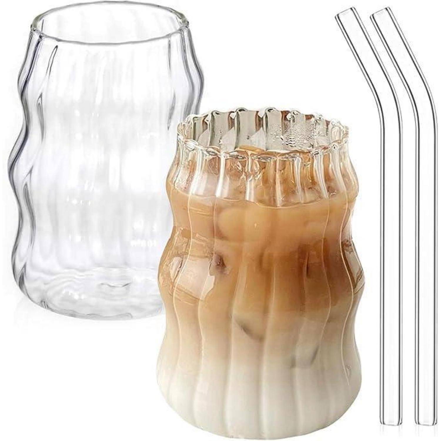 Transparente, welliges Glastasse mit Eiskaffee und Sahne, zusammen mit einer zweiten leeren Tasse und zwei wiederverwendbaren Glasstrohhalmen gezeigt.
