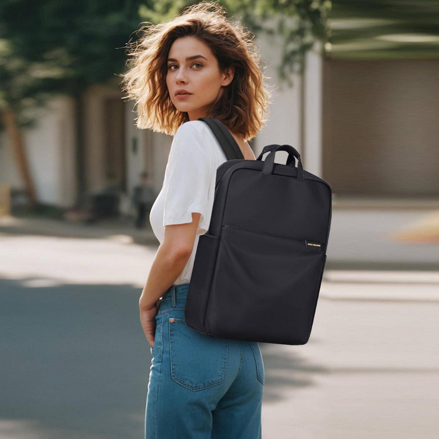 Junge Frau, die draußen mit einem schwarzen Rucksack spaziert, trägt ein weißes T-Shirt und blaue Jeans, blickt zurück zur Kamera.