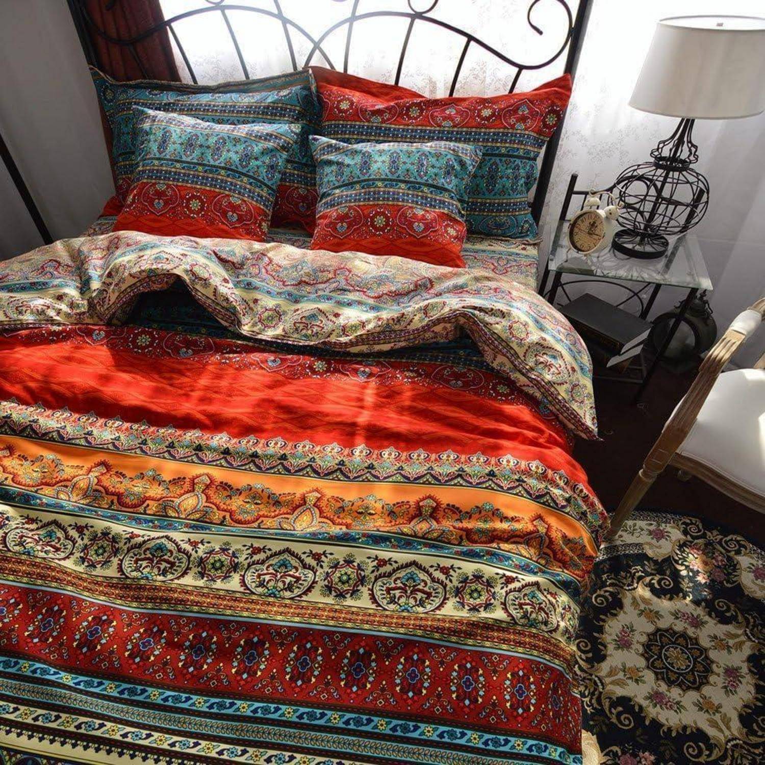 Buntes gemustertes Bett mit Kissen und einer Decke, neben einem weißen Nachttisch mit Lampe und Uhr in einem Schlafzimmer.