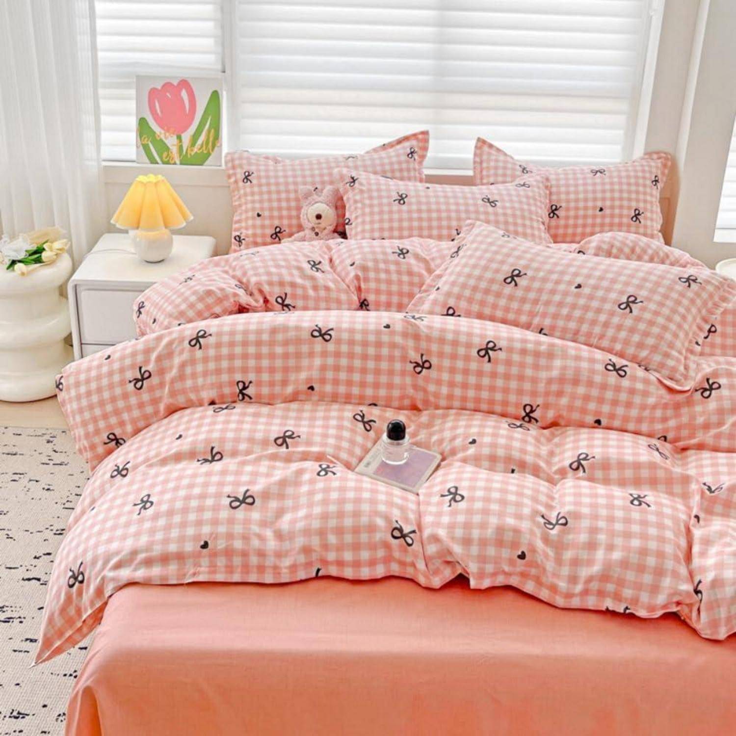 Rosa Gingham-Bett mit Schleifenmuster-Bettwäsche und passenden Kissen in einem hellen Schlafzimmer, mit einer Korallendecke und einer Nachttischlampe.