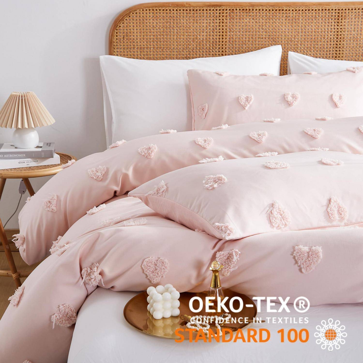 Rosa gemusterter Bettbezug auf einem Bett mit weißen Kissen und einem gewebten Kopfteil, mit einem Zertifizierungsabzeichen „OEKO-TEX STANDARD 100