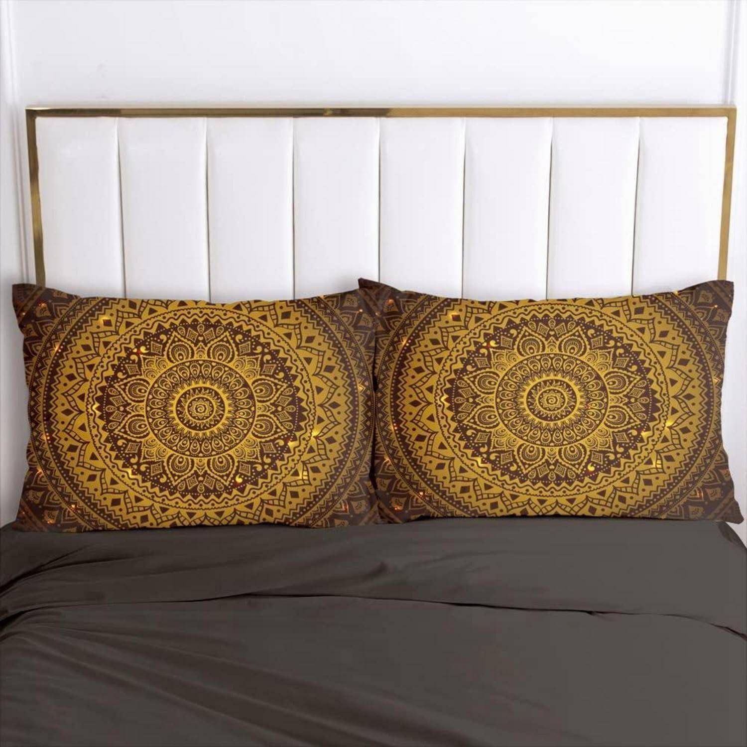 Bett mit weiß gepolstertem Kopfteil, zwei passenden braun-goldenen Mandala-Kissen und einer dunkelgrauen Decke.