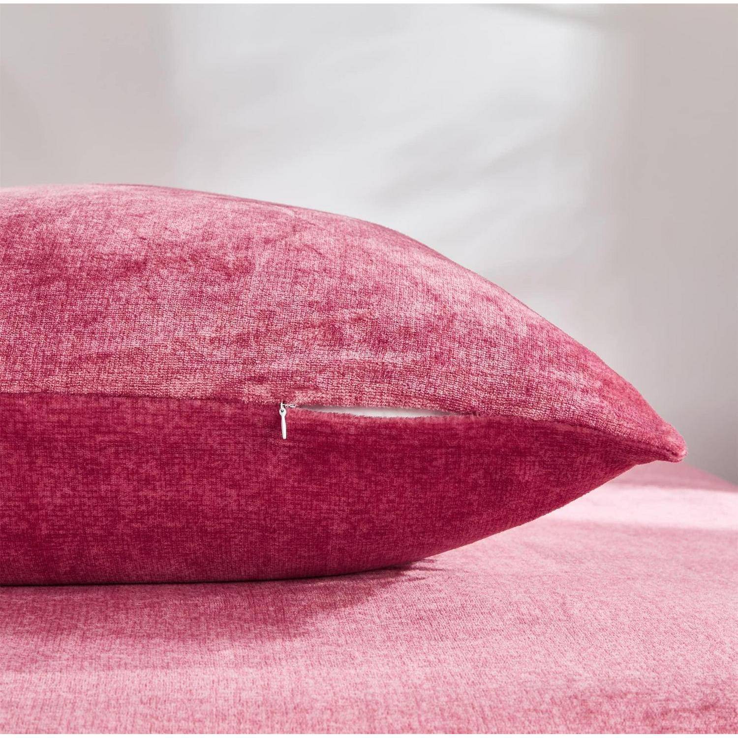 Rosa strukturiertes Dekokissen auf einem rosa Sofa oder Bett vor einer hellen Wand, mit einem kleinen Reißverschluss auf der Seite sichtbar.