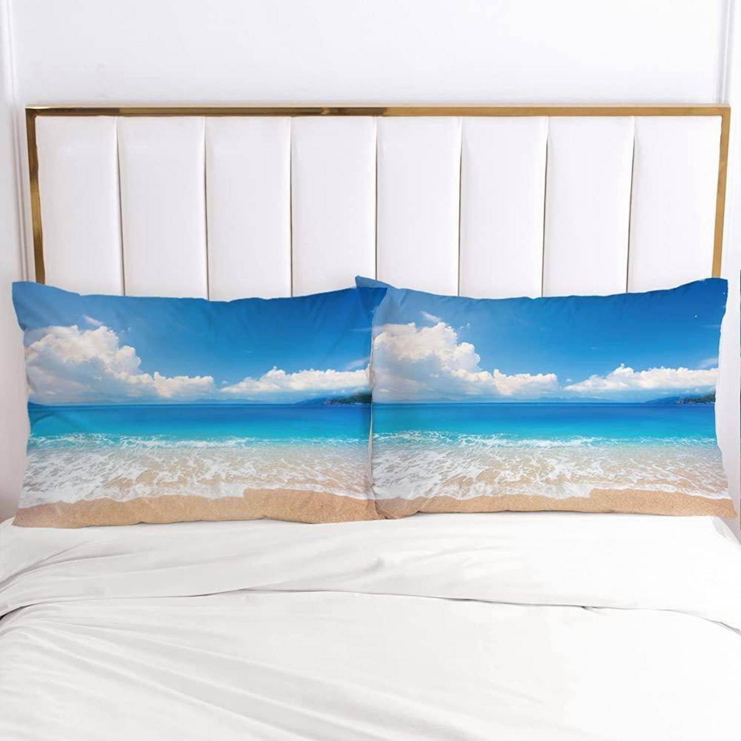 Weißes Bett mit zwei Kissen mit Ozean-Strand-Druck gegen ein weißes Kopfende.