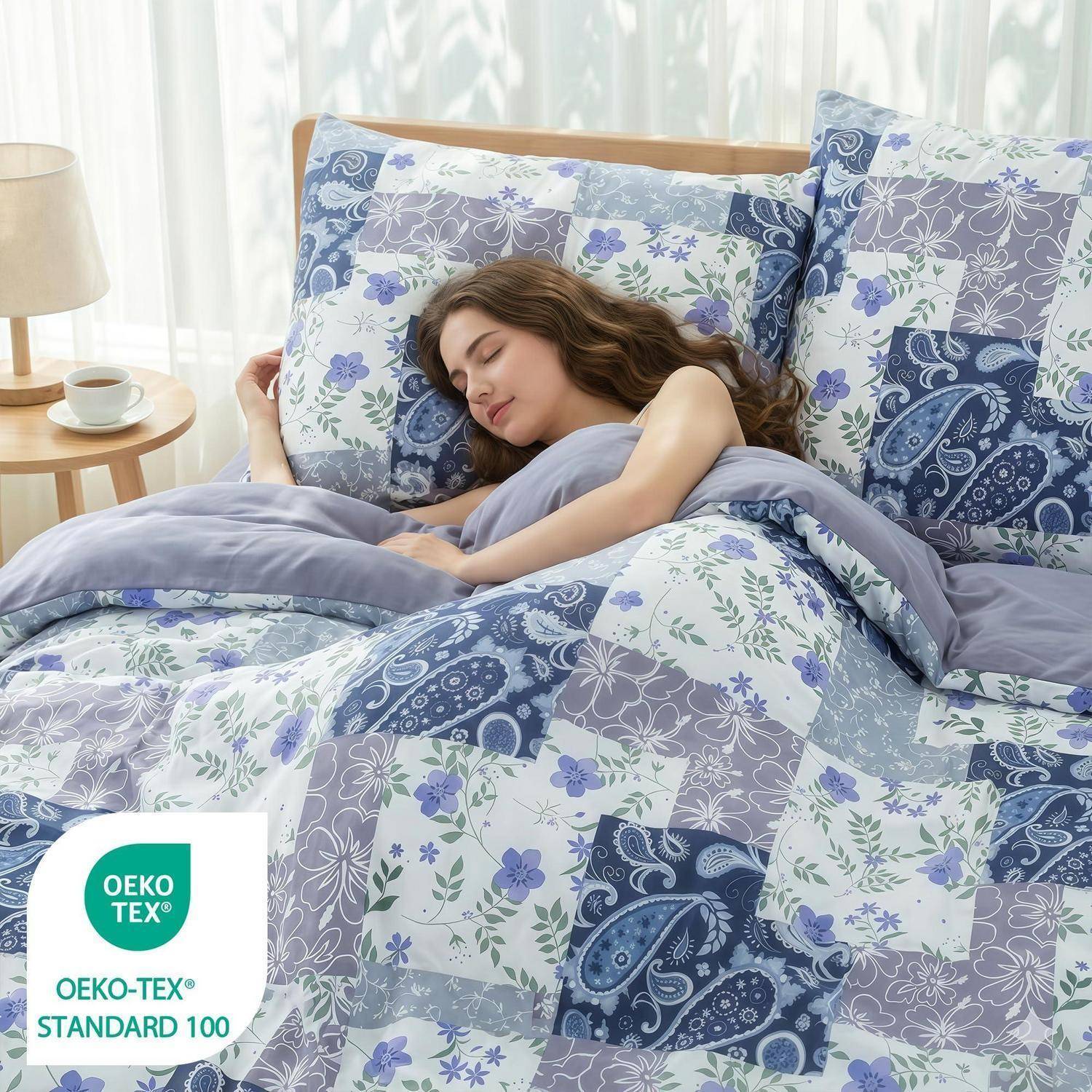 Schlafende Frau unter blauer und lavendelfarbener floraler Patchwork-Bettwäsche in einem sonnigen Schlafzimmer, mit sichtbarem OEKO-TEX Standard 100 Etikett.