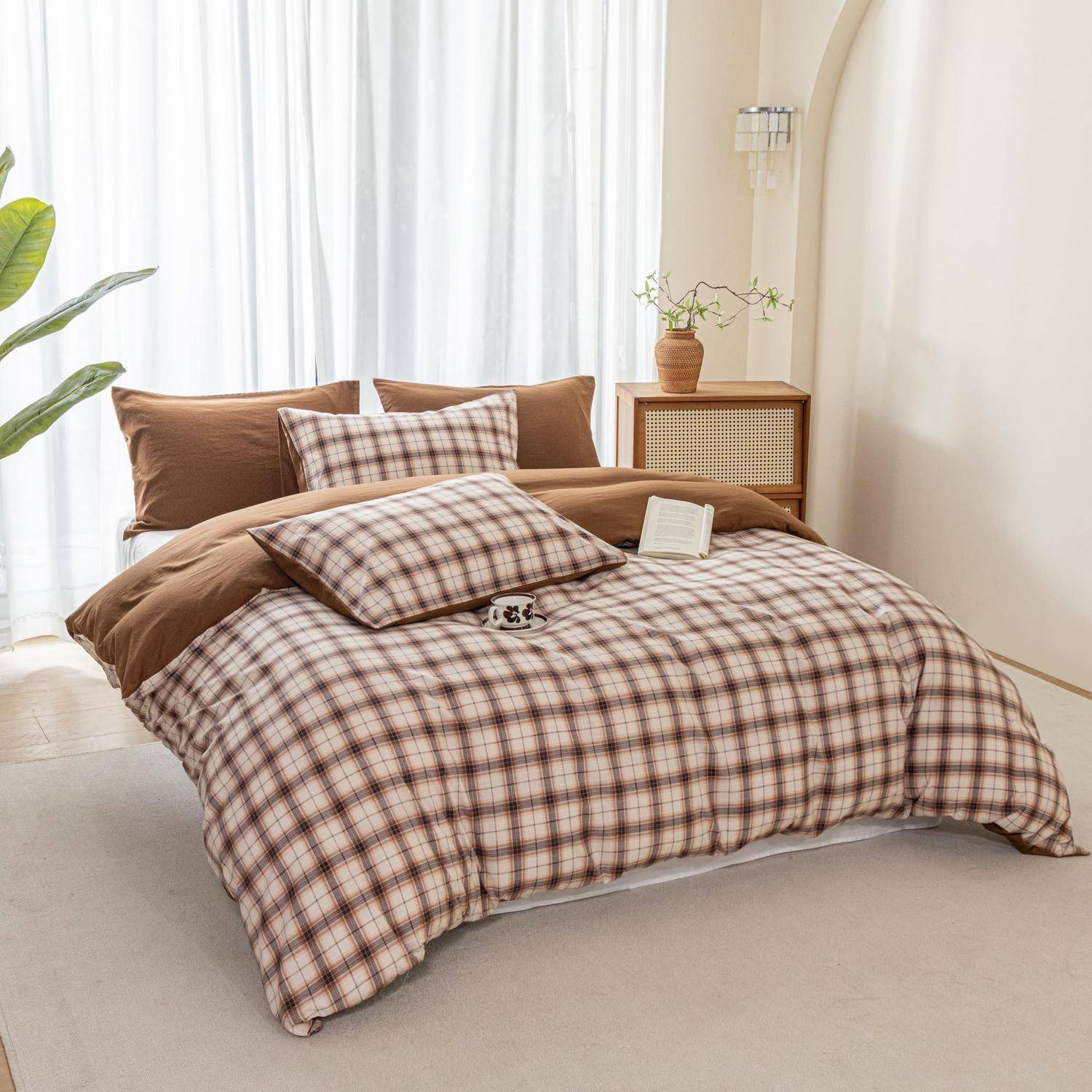 Ordentlich gemachtes Bett mit braunem Karomuster-Bettwäsche, Kissen, einem aufgeschlagenen Buch und einem kleinen Nachttisch in einem hellen Schlafzimmer.