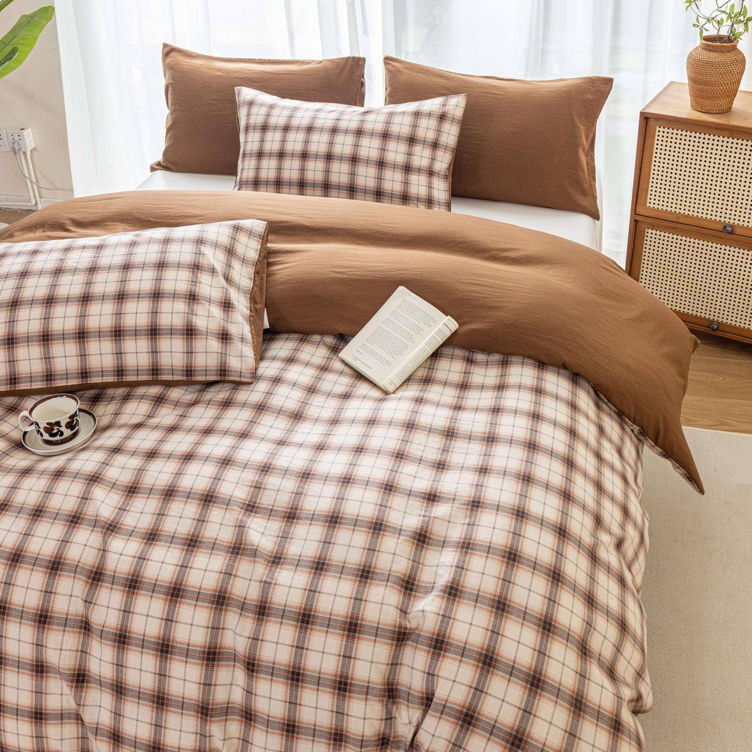 Braun kariertes Bettwäsche-Set auf einem ordentlich gemachten Bett, mit passenden Kissen, einem Buch und einer Tasse auf dem Nachttisch in einem hellen Schlafzimmer.