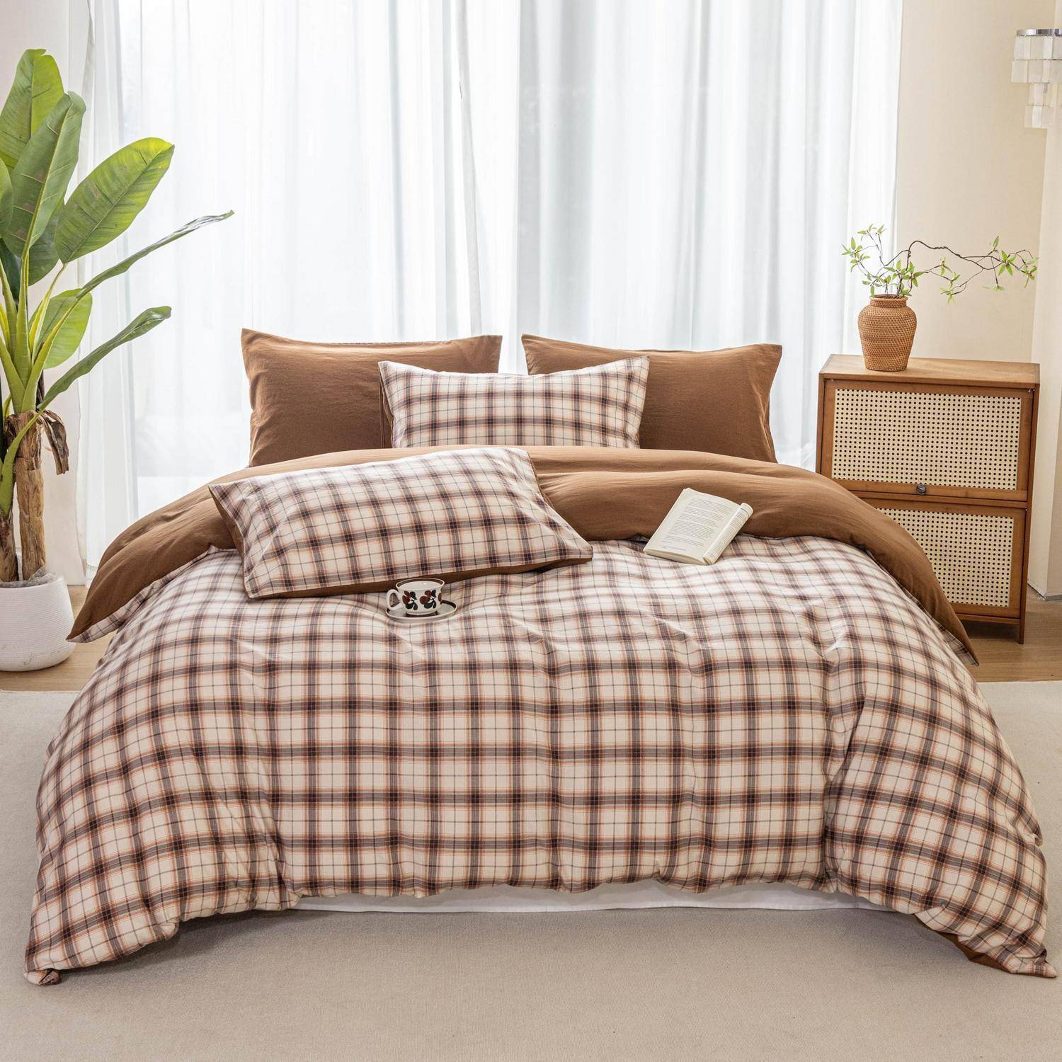 Ein ordentlich gemachtes Bett mit brauner und karierter Bettwäsche in einem hellen Schlafzimmer, flankiert von einer Topfpflanze und einem kleinen Nachttisch.