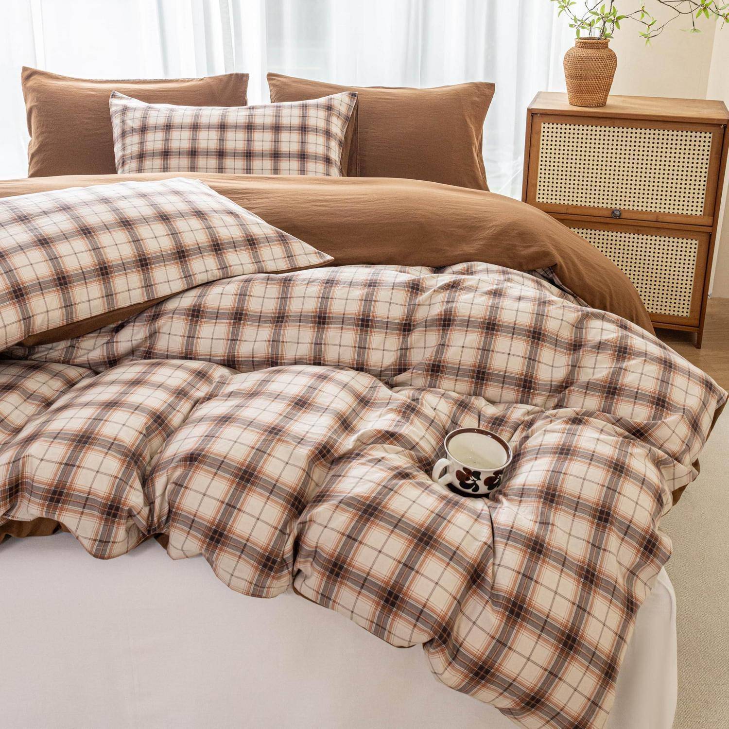 Kariertes Bett- und Kissenbezug-Set in Beige und Braun auf einem ordentlich gemachten Bett, mit passenden Kissen, einer Tasse auf der Steppdecke und einem Holznachttisch im Hintergrund.