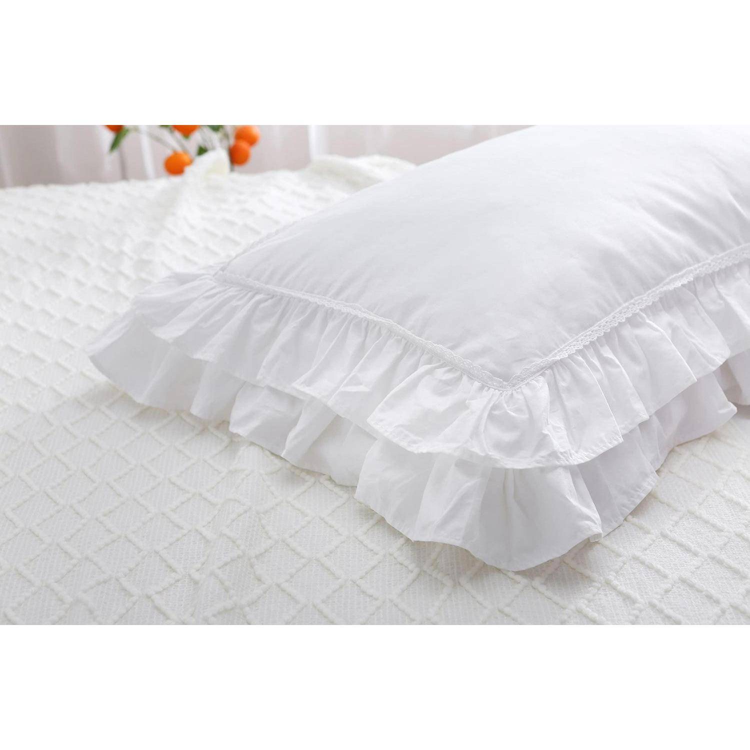 Weiß gerüschtes dekoratives Kissen auf einer strukturierten weißen Tagesdecke in einem hellen Schlafzimmer.