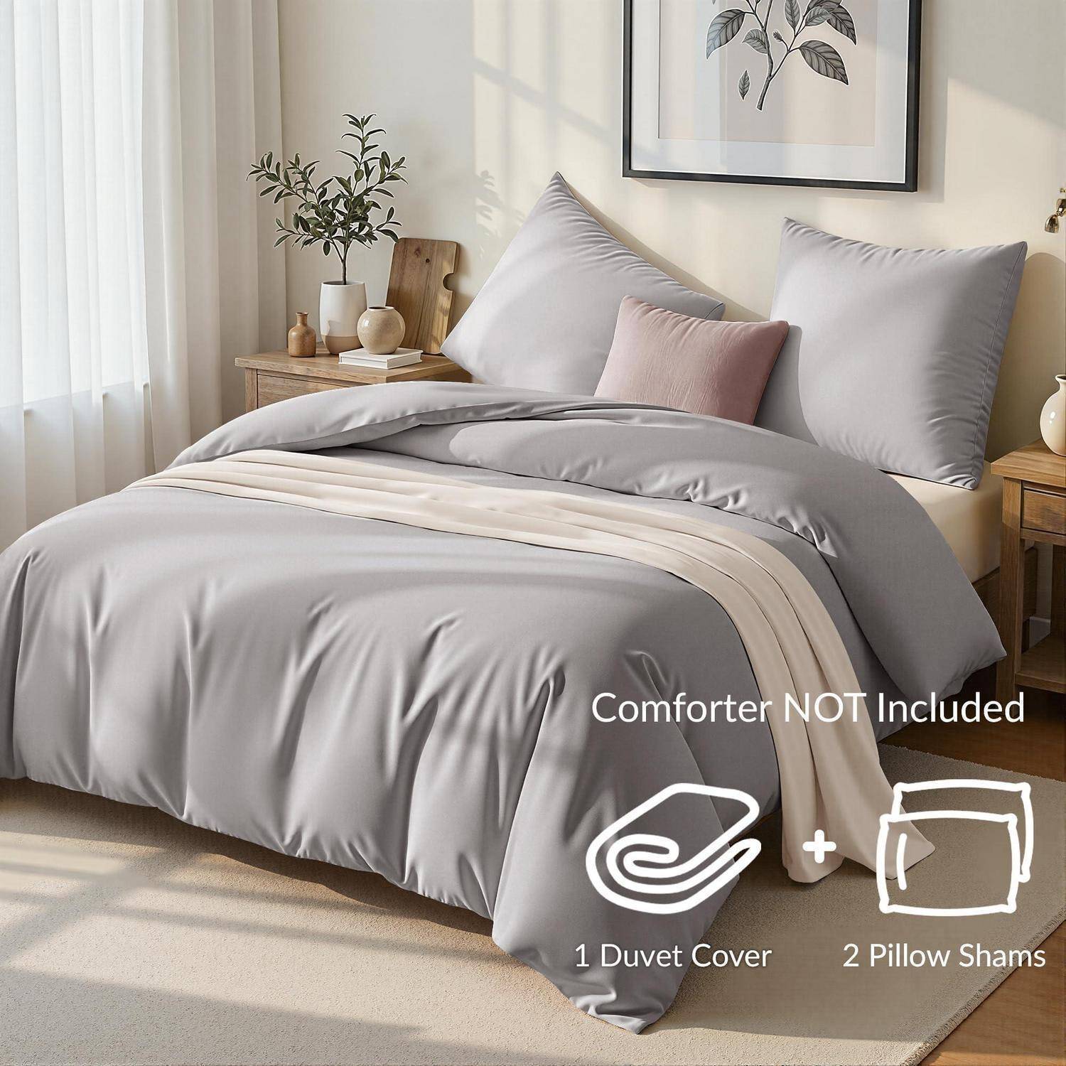 Bett mit grauem Daunendeckenbezug und zwei Kissenbezügen in einem hellen Schlafzimmer; der Text besagt „Daunendecke NICHT enthalten" und enthält Symbole für 1 Daunendeckenbezug und 2 Kissenbezüge.