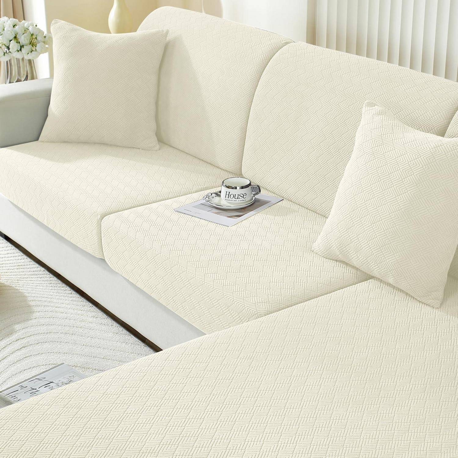 Cremefarbenes Sofa mit passenden Kissen in einem hellen Wohnzimmer, mit einer Kaffeetasse und einem Buch auf dem Sitz.
