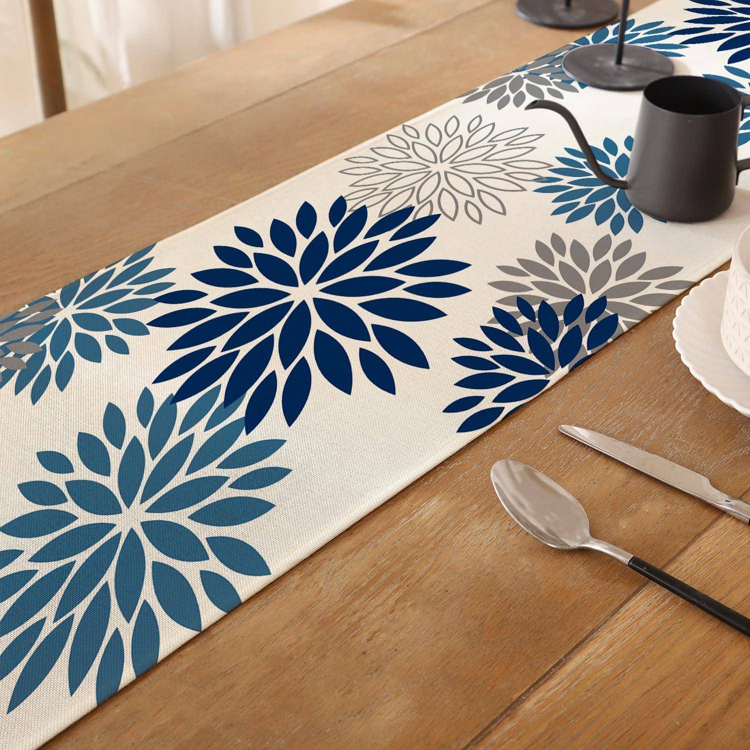 Blauer und grauer Blumen-Tischläufer auf einem Holzesstisch mit einer Tasse, Tellerrand und Besteck in der Nähe.