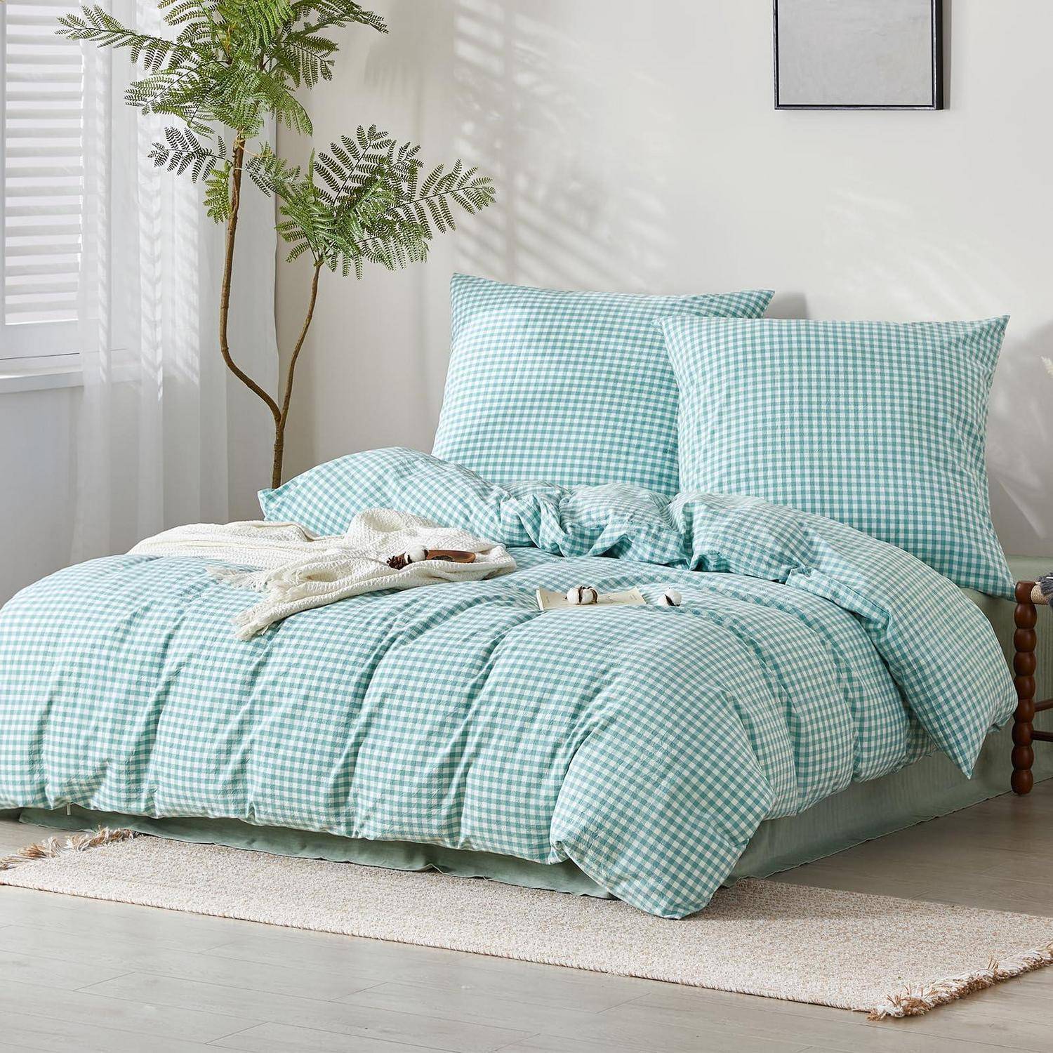 Bett mit hellblauem Gingham-Bettwäsche und Kissen in einem hellen, minimalistischen Schlafzimmer mit einer Topfpflanze, Fenster und Teppich.