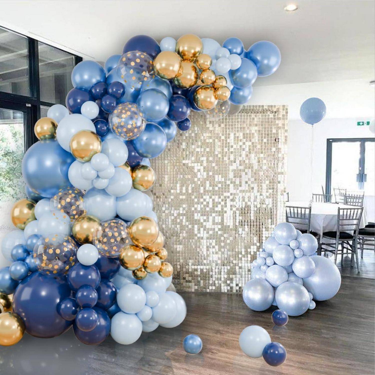 Innenparty-Setup mit einem großen Ballonbogen in Blau, Weiß und Gold, einer Paillettenkulisse in Gold und Ballongruppen auf dem Boden.