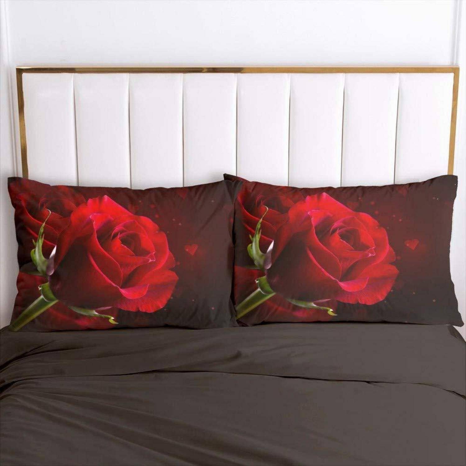 Bett mit dunkler Bettwäsche und zwei passenden Kissen mit großen roten Rosen bedruckt vor einem weiß gepolsterten Kopfteil.