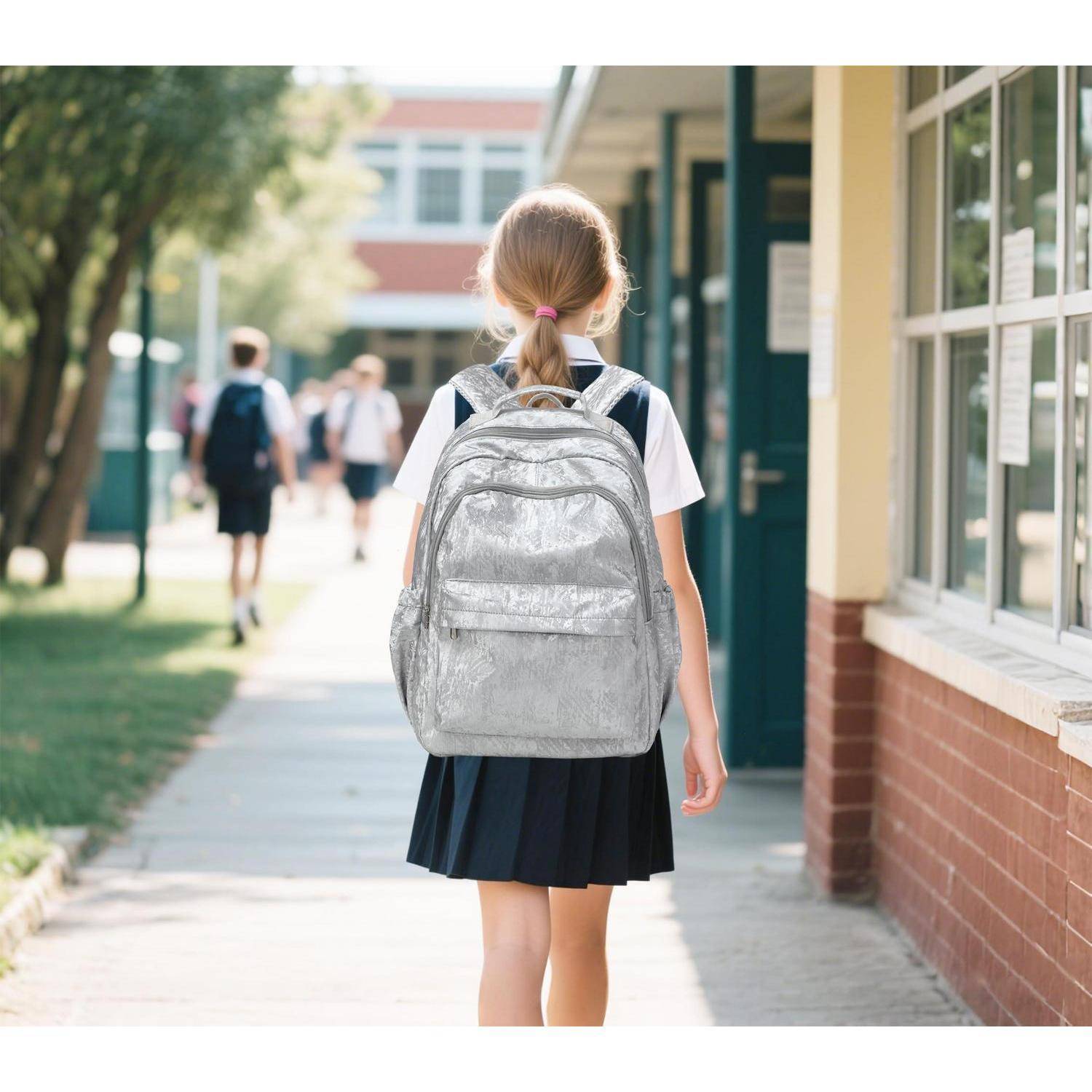 Ein Schulmädchen mit einem silbernen Rucksack geht einen Schulweg entlang, während andere Schüler weiter vorne in der Nähe des Gebäudes sind.