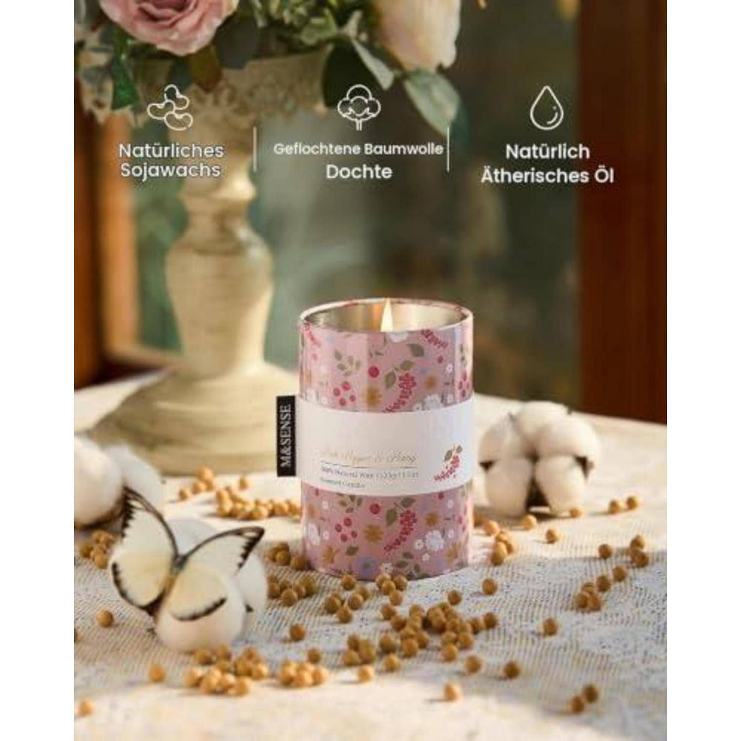 Dekorative Kerze in einer rosa Blumenblechdose auf einem Tisch mit Baumwollkapseln; deutscher Text hebt natürliches Sojawachs, geflochtener Baumwolldocht und natürliches ätherisches Öl hervor.