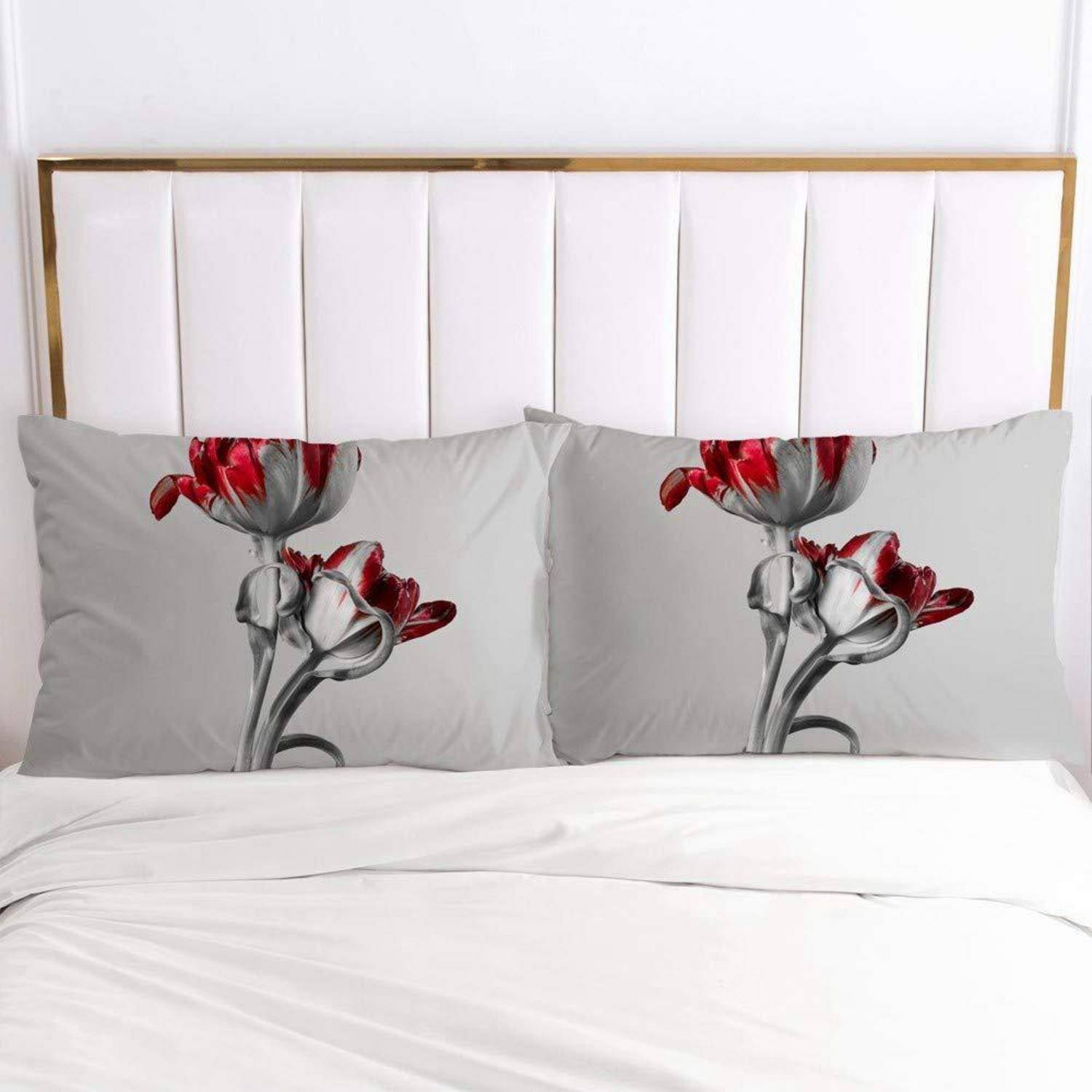 Ein ordentlich gemachtes Bett mit zwei grauen Blumenkissen mit roten und weißen Blumendruck vor einem weiß gepolsterten Kopfteil.