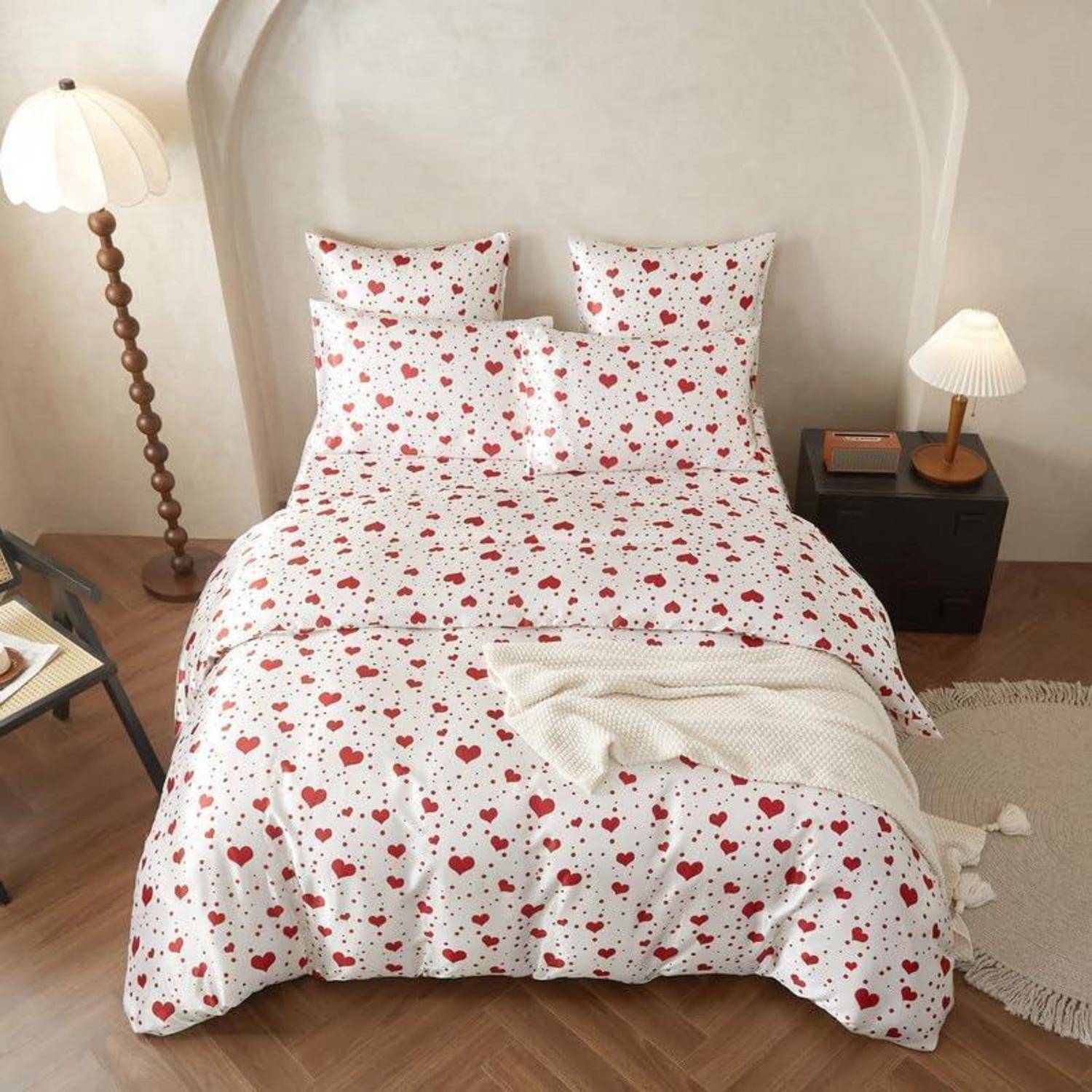 Ein ordentlich gemachtes Bett mit weißer Bettwäsche, bedeckt mit roten Herzen, flankiert von zwei Nachttischlampen in einem gemütlichen Schlafzimmer.