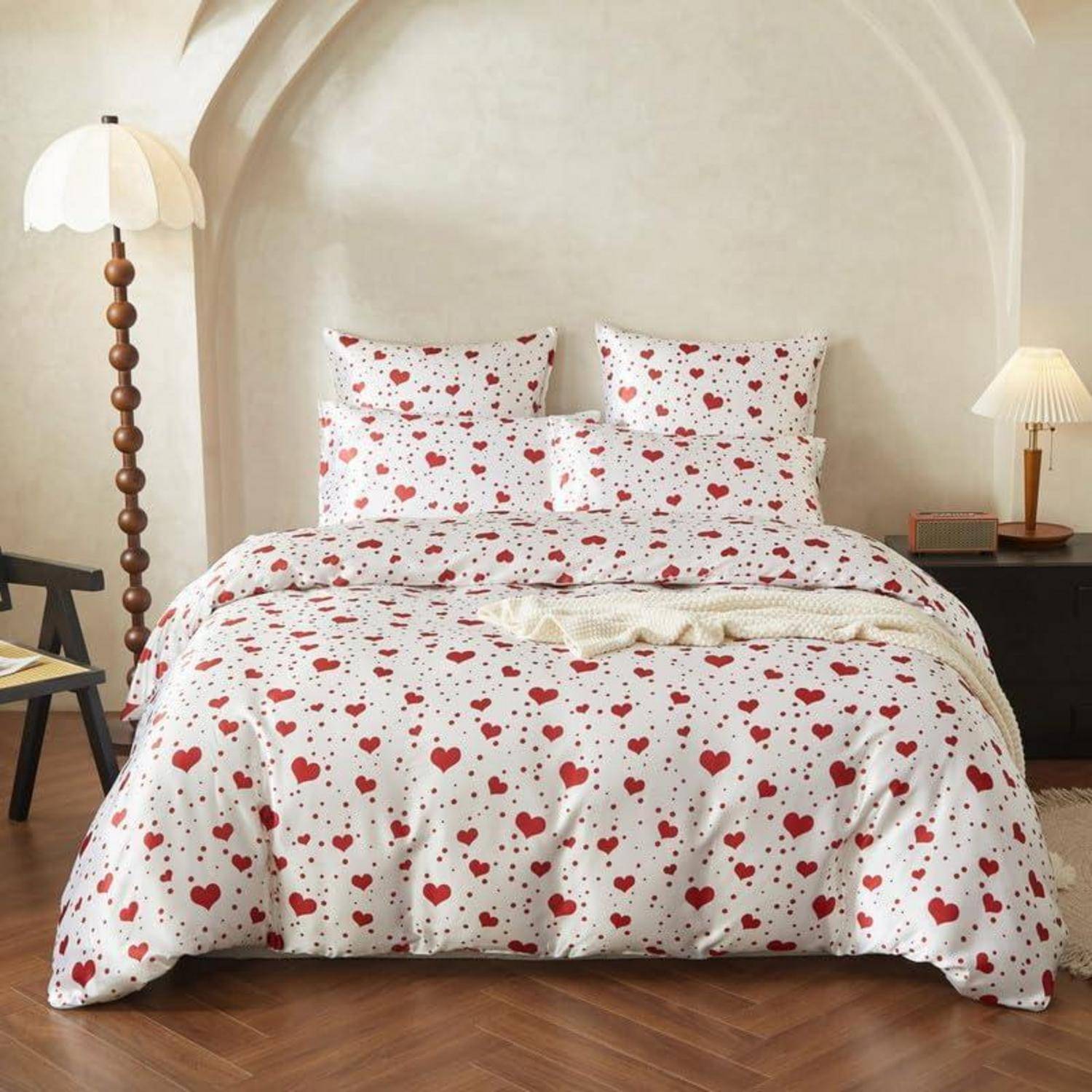 Bett mit weiß gemusterter Bettdecke mit Herzenmuster und passenden Kissen in einem gemütlichen Schlafzimmer mit Bogenwand, Stehlampe und Nachttisch.