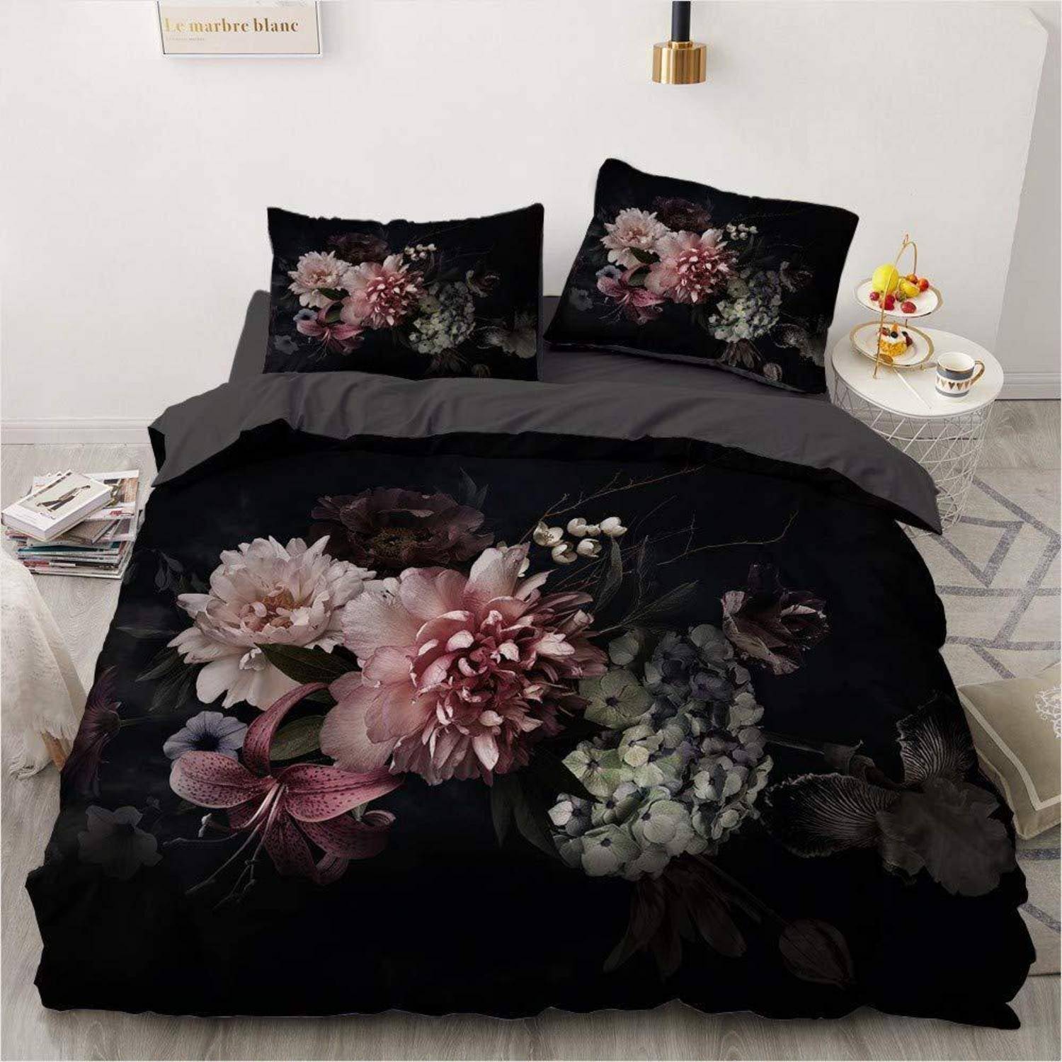 Schwarzes Blumenbettwäscheset auf einem Bett, mit passenden Kissenbezügen und Bettdeckenbezug mit großen rosa und weißen Blüten.
