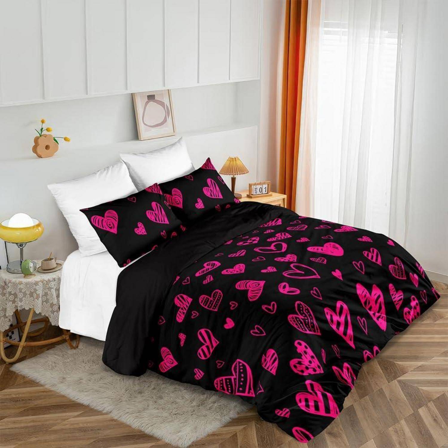 Bett in einem hellen Schlafzimmer mit einer schwarzen Steppdecke und Kissen mit rosa Herzmustern, weißen Laken und Vorhängen.