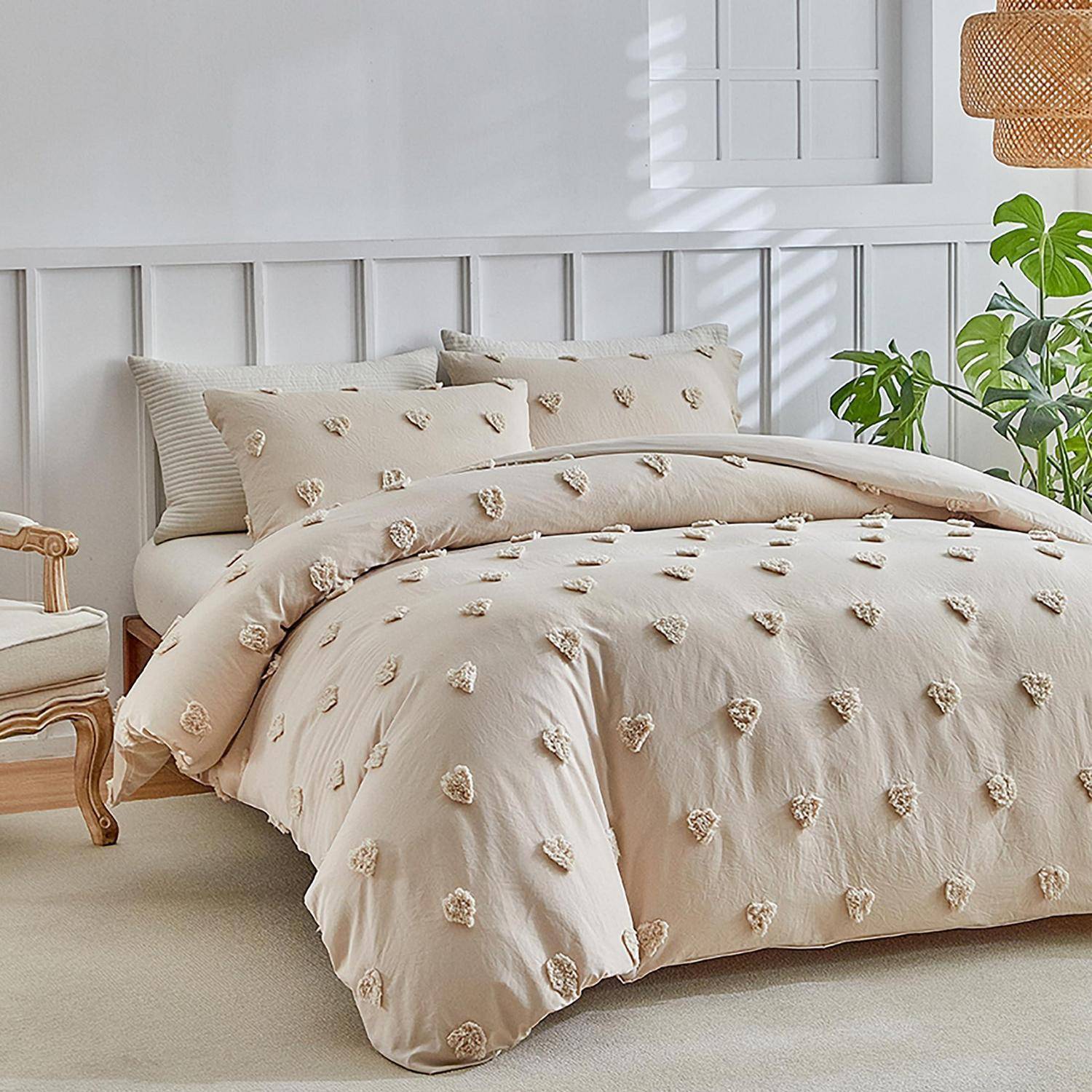 Beige gesteppte Bettdecke auf einem Bett in einem hellen, minimalistischen Schlafzimmer mit Kissen, weißem Kopfteil und Zimmerpflanzen.