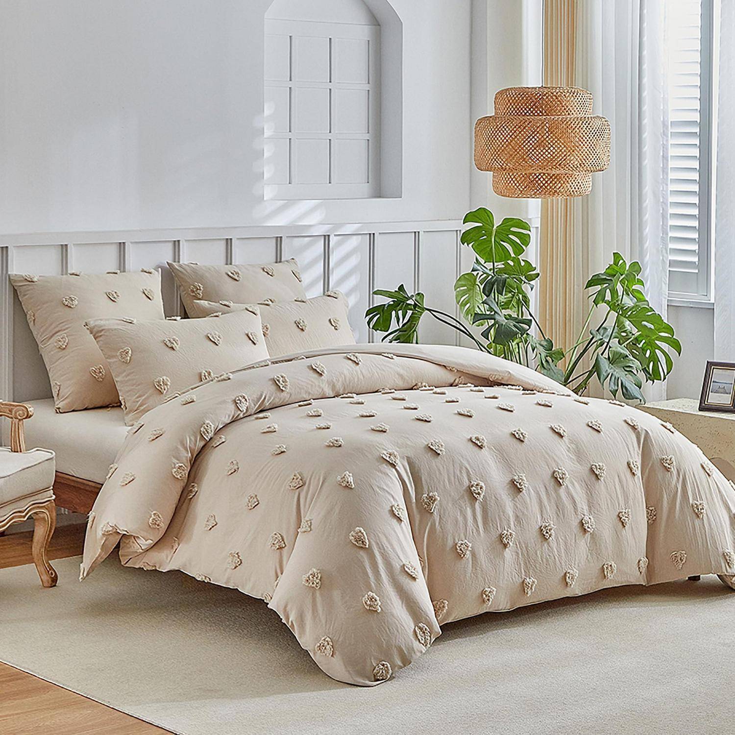 Helles Schlafzimmer mit einem ordentlich gemachtem Bett in beige strukturiertem Bettzug, Pflanzen am Fenster und einer geflochtenen Pendelleuchte.