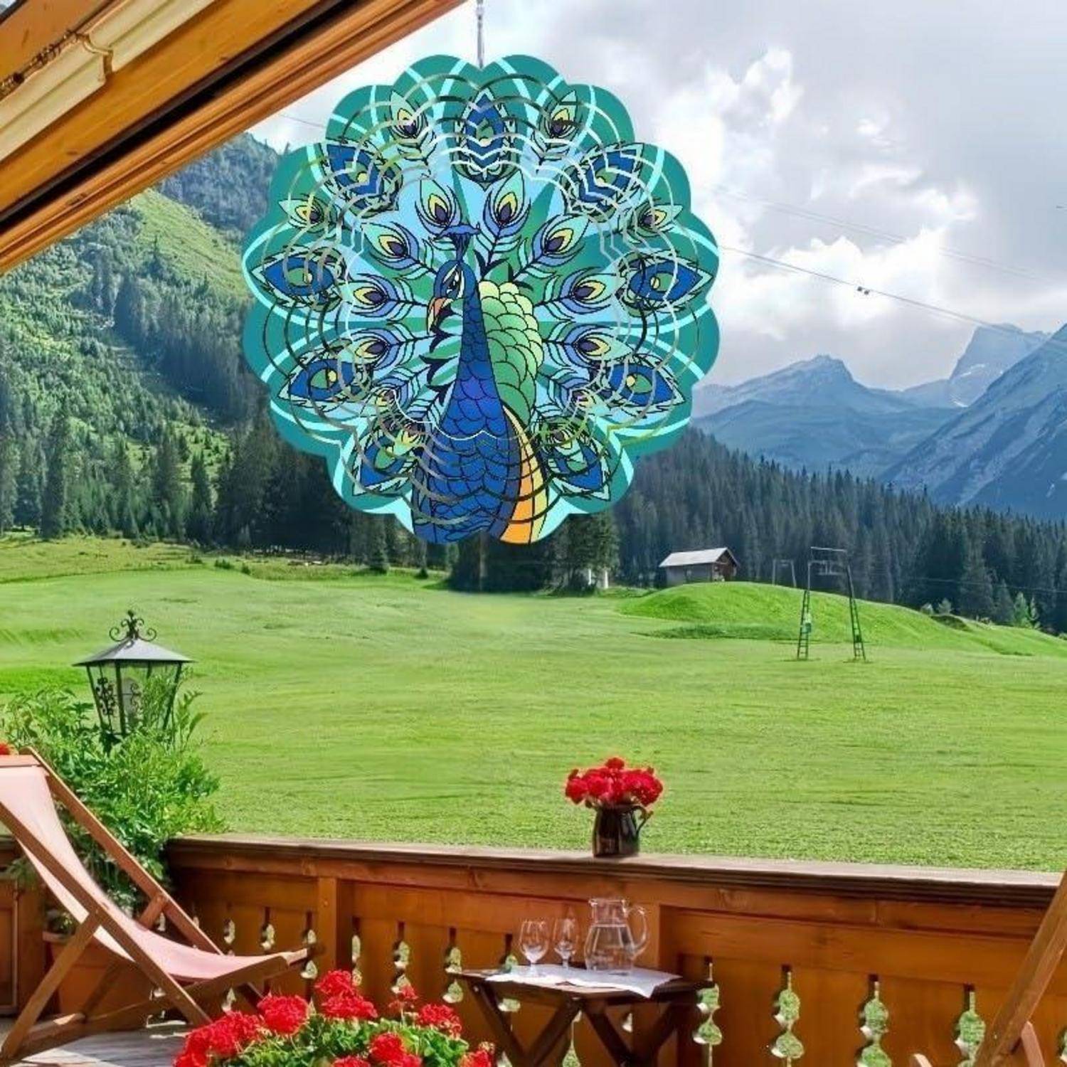 Großer Pfau-Windspinner, der über einem Balkon hängt und überblickt eine grüne Bergwiese mit roten Blumen, einen Holzstuhl und entfernte Gipfel.