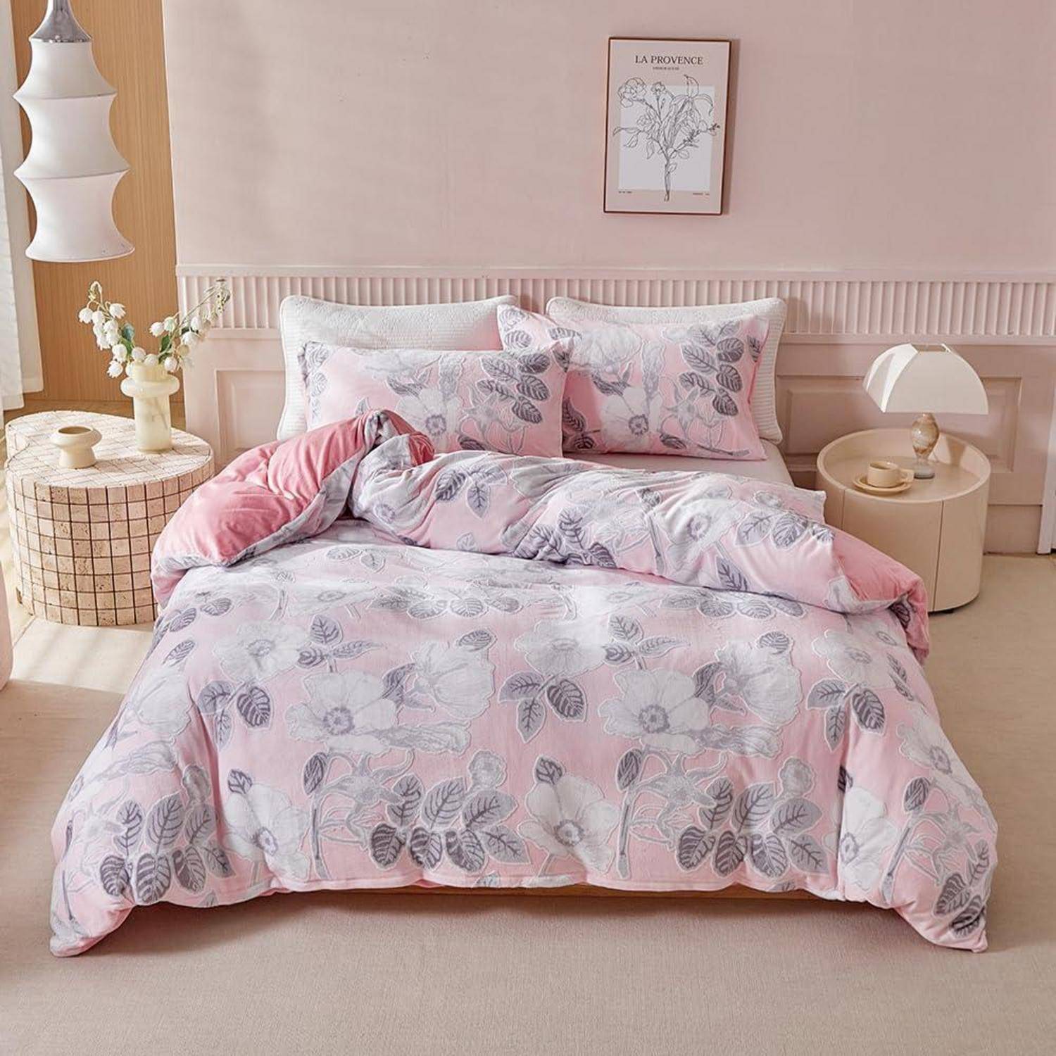 Ein ordentlich gemachtes Bett mit rosa Blumenbettwäsche und Kissen in einem weichen, minimalistischen Schlafzimmer, flankiert von runden Nachttischen und Lampen.