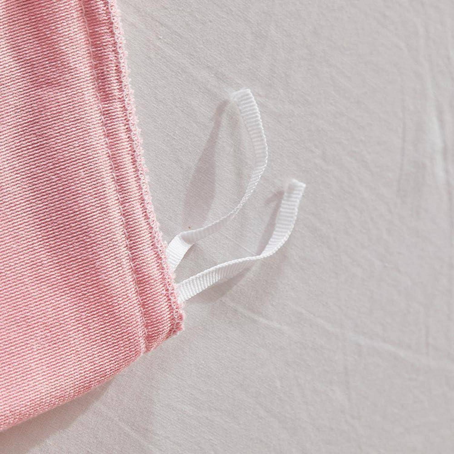 Nahaufnahme eines rosa Stoffbeutels oder einer Maske mit zwei weißen elastischen Schlaufen auf hellem Hintergrund.